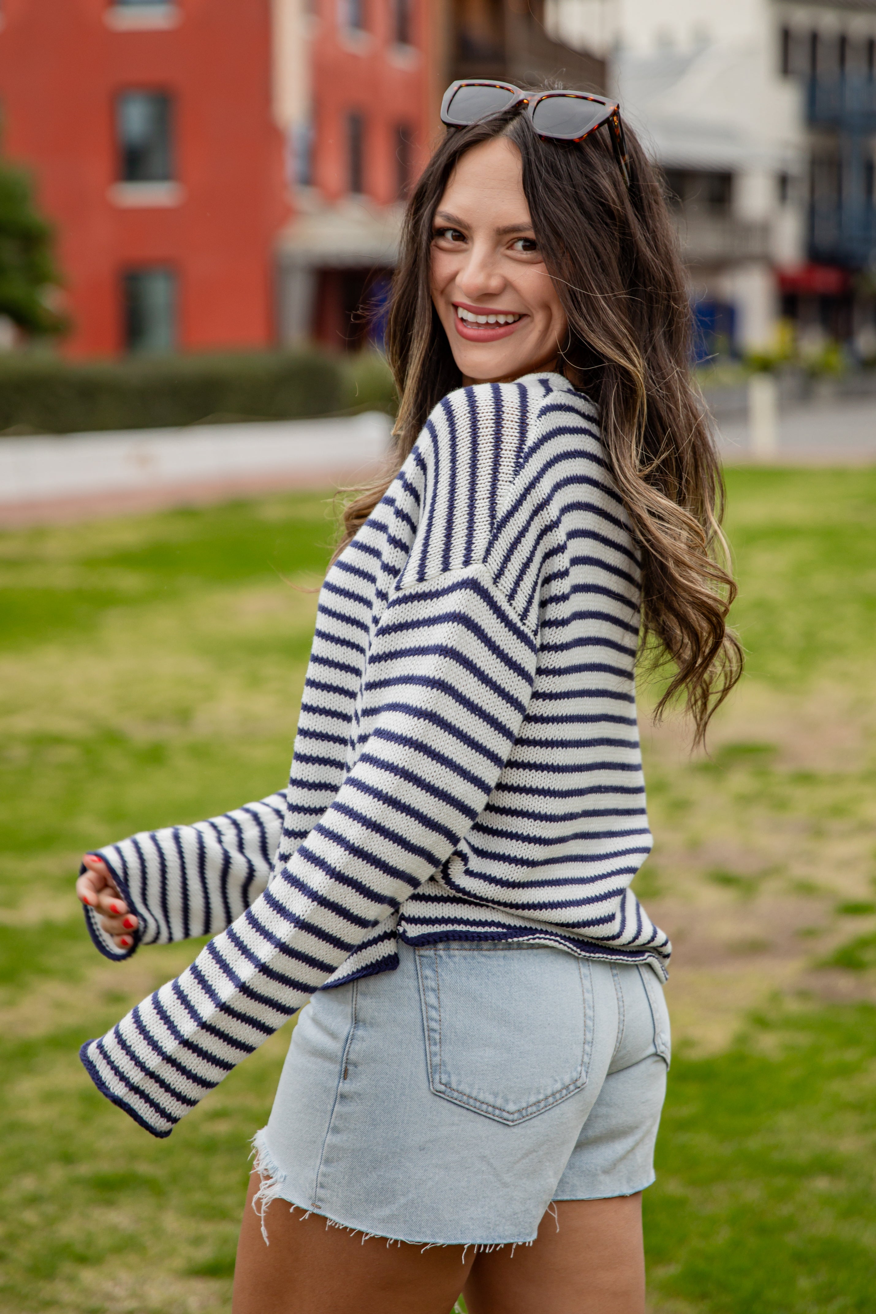 Woman wearing a striped sweater and denim shorts standing outdoors with buildings in the background
