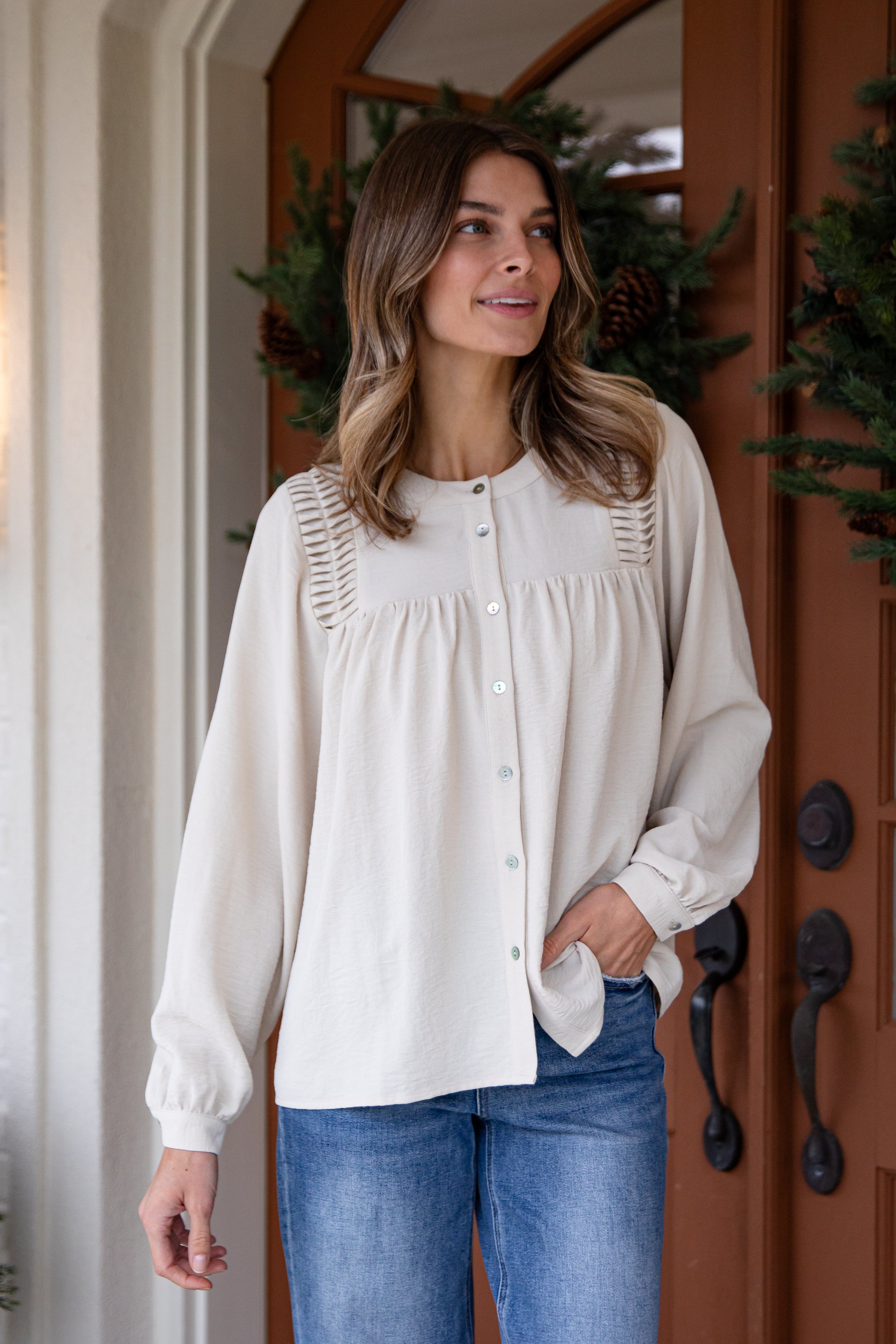 Woman wearing a white blouse and blue jeans standing in front of a wooden door with decorative elements.