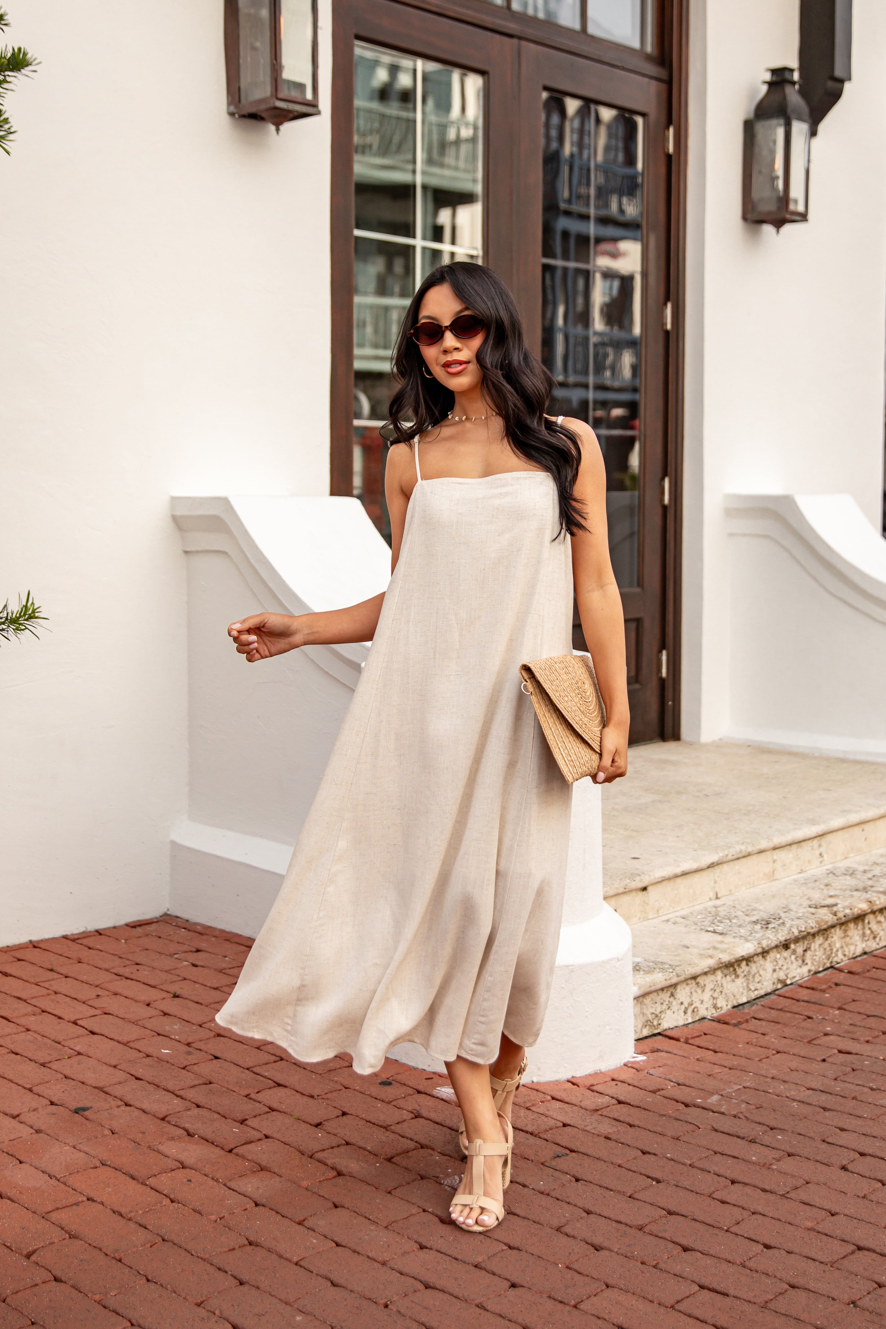 Woman in a beige dress walking on a brick path outside a building.