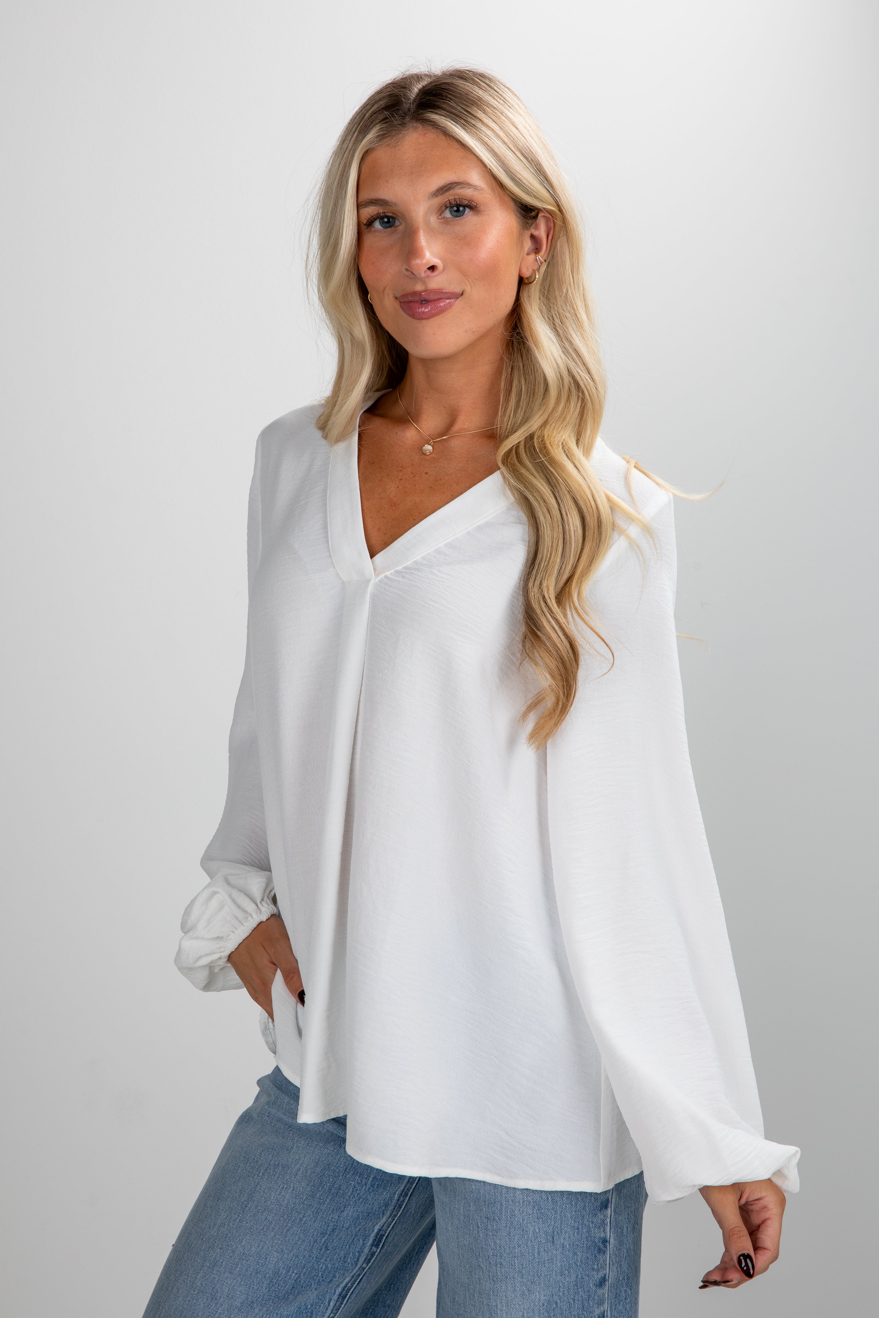 Woman wearing a white blouse and blue jeans against a plain background