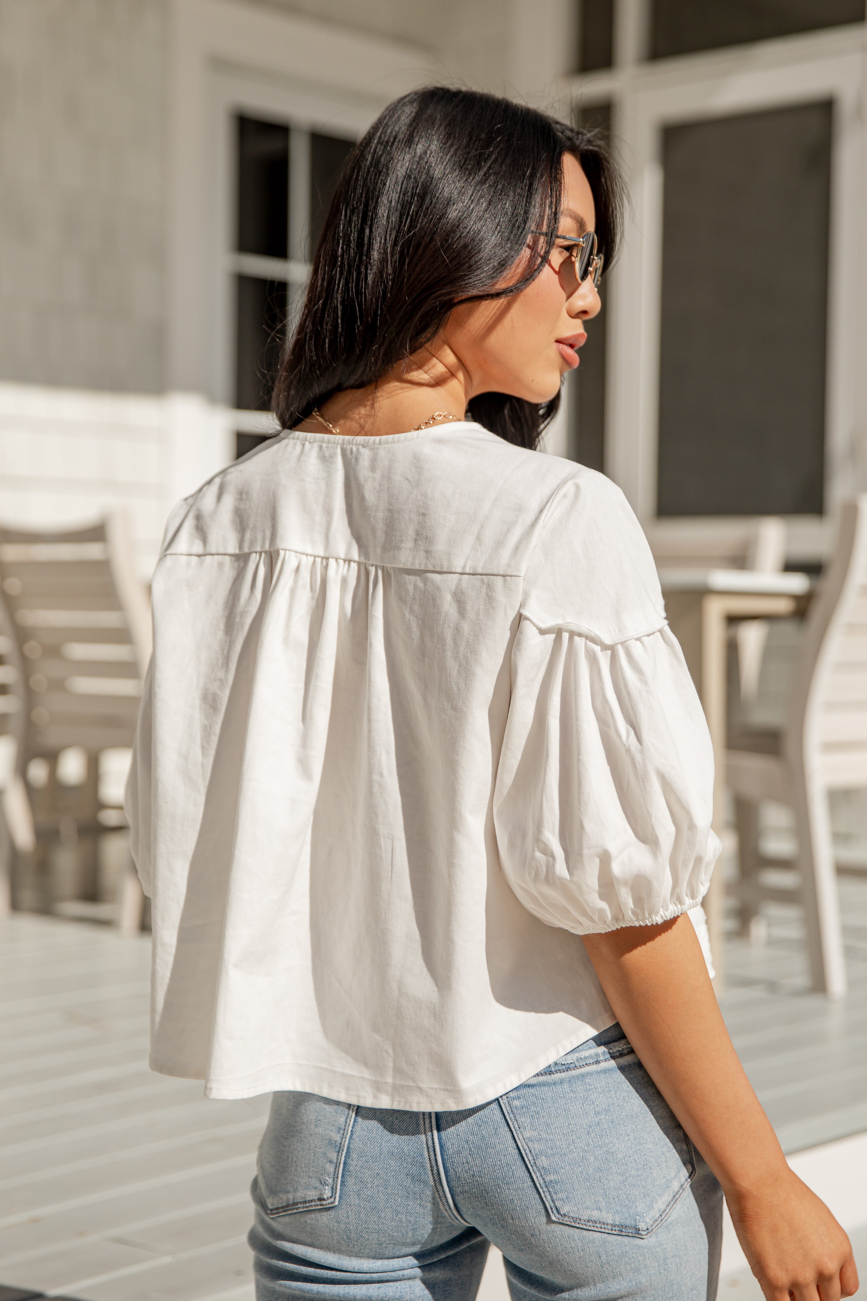Woman wearing a white blouse and light blue jeans outdoors.