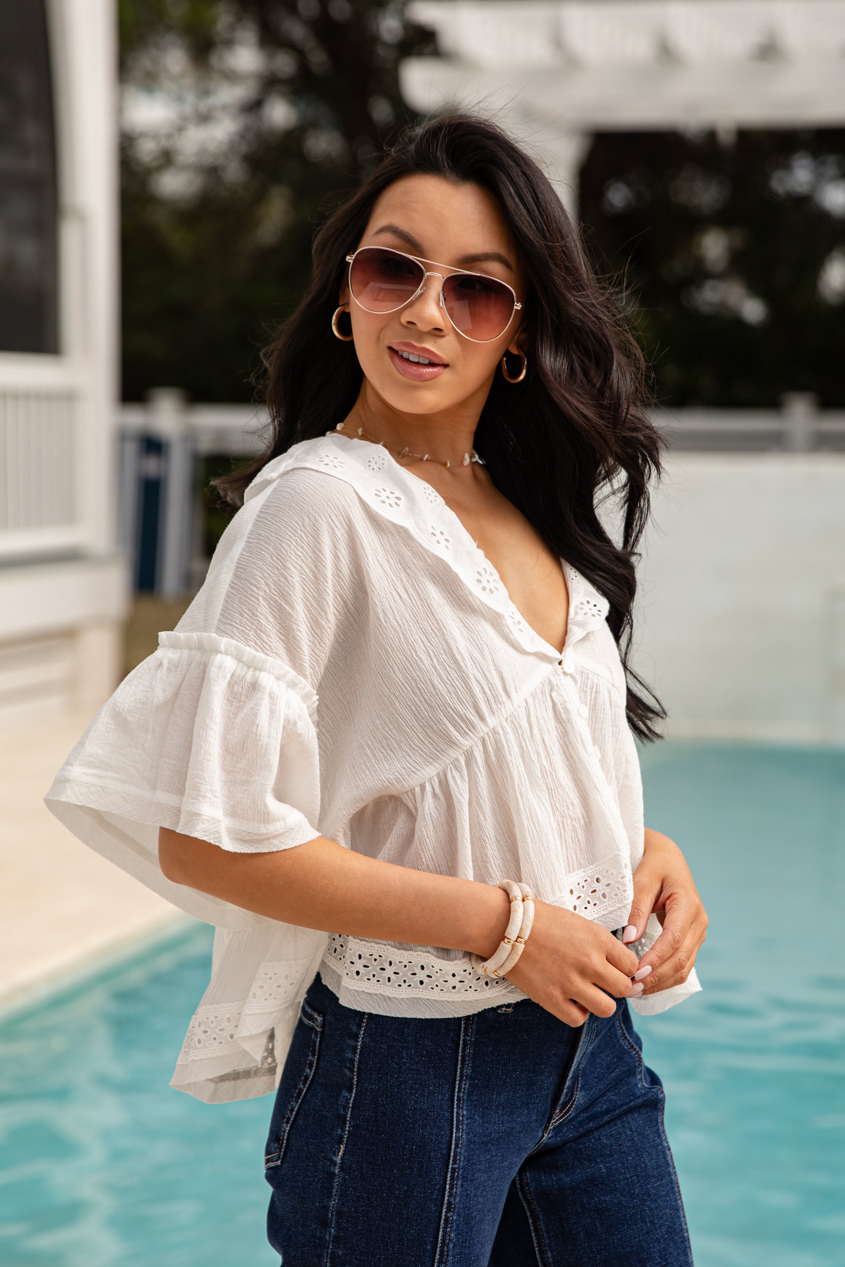 Woman wearing a white blouse and sunglasses by a pool