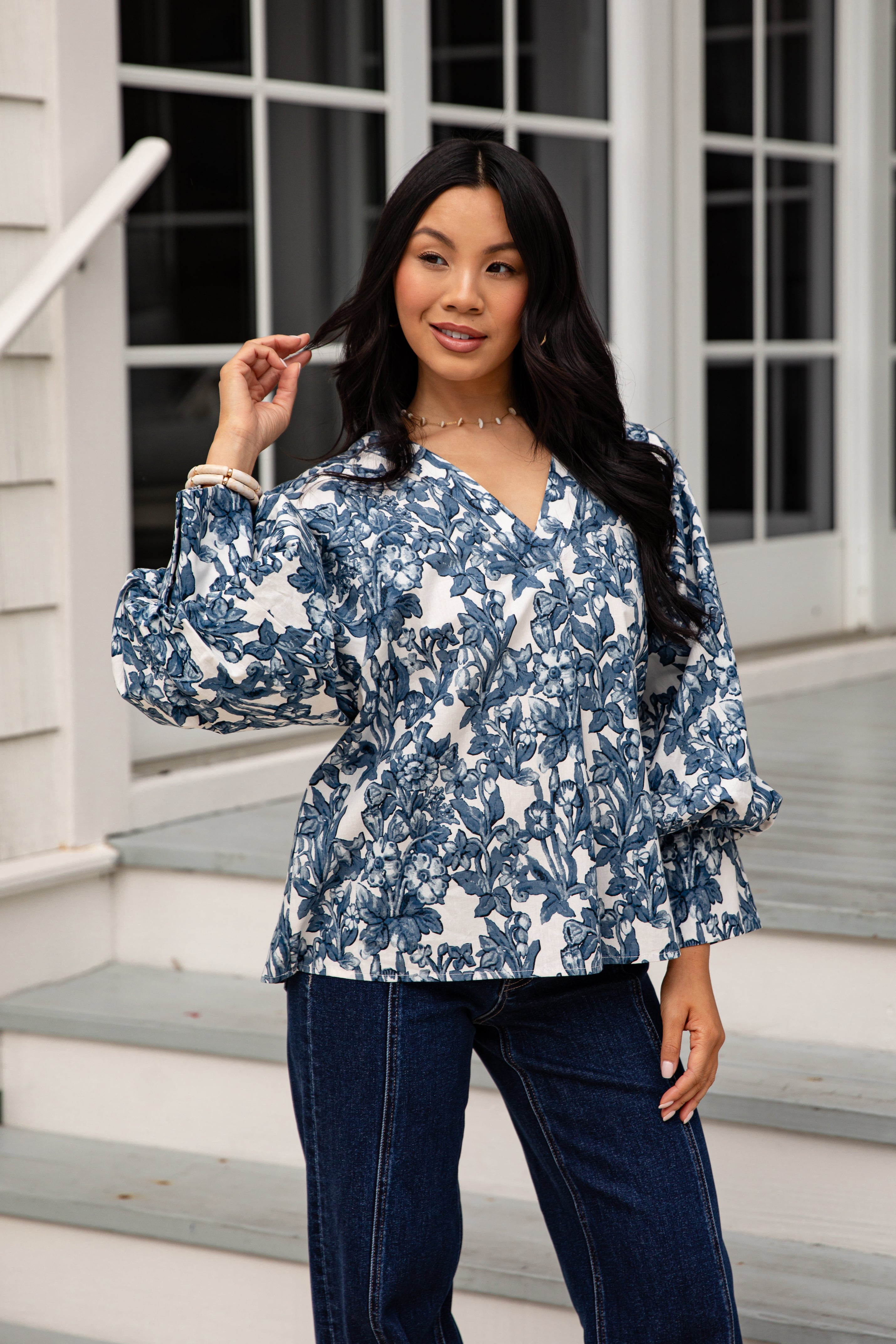 Woman wearing a blue floral blouse and dark jeans standing on steps.