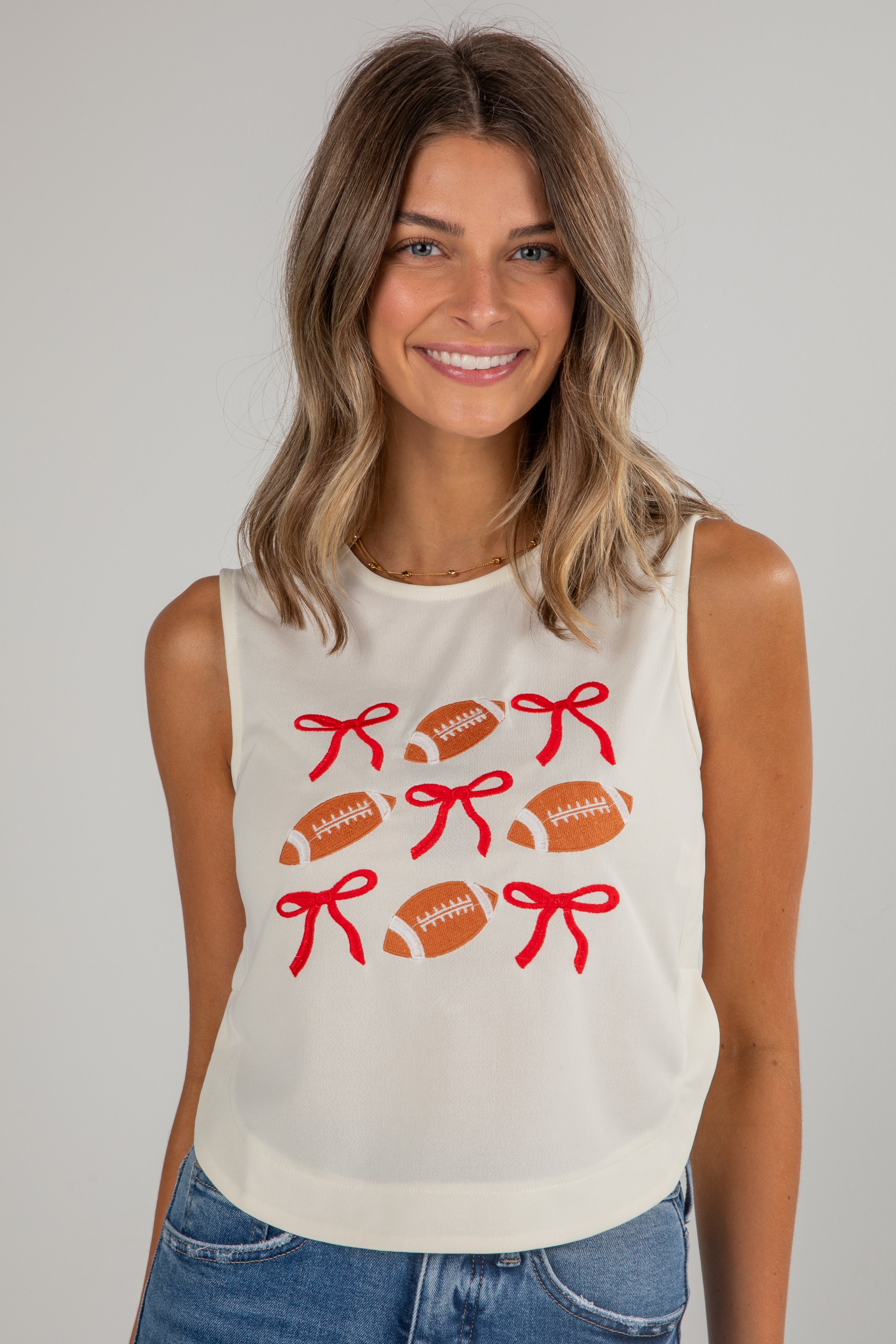 Woman wearing a sleeveless shirt with football and bow designs on a plain background
