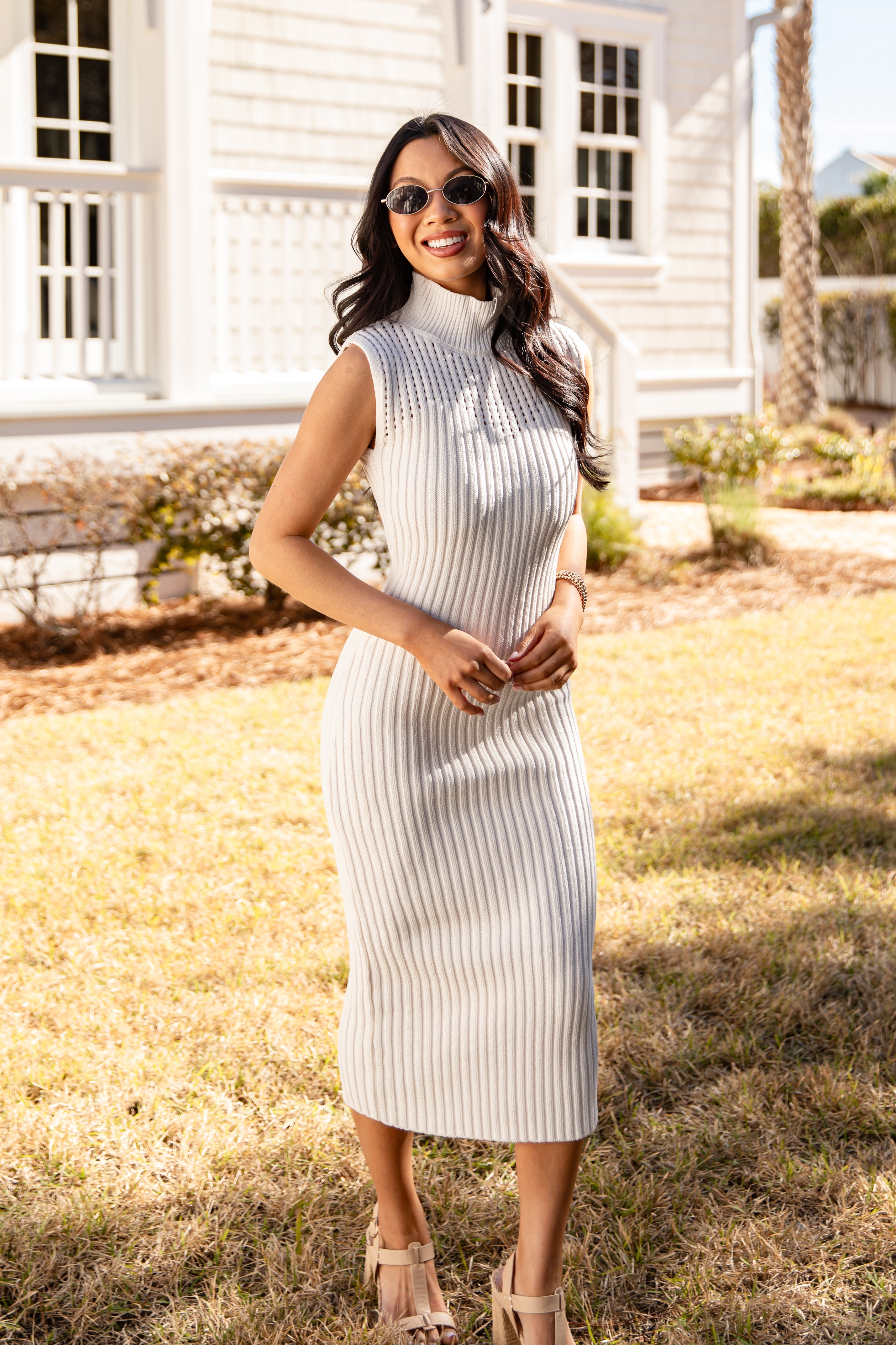 Woman in a white ribbed dress standing outdoors with a house and palm tree in the background