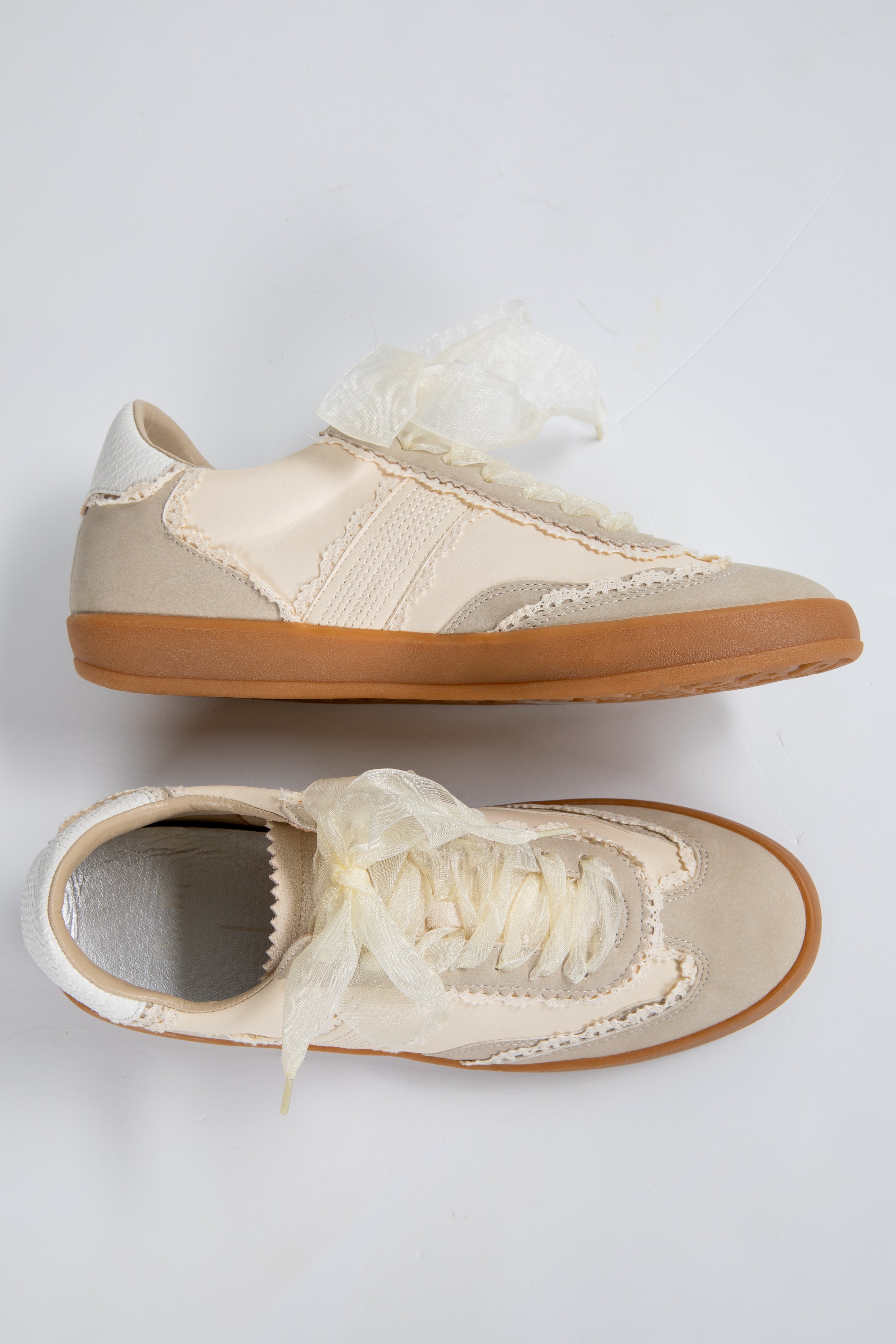 Pair of beige sneakers with white laces on a light gray background