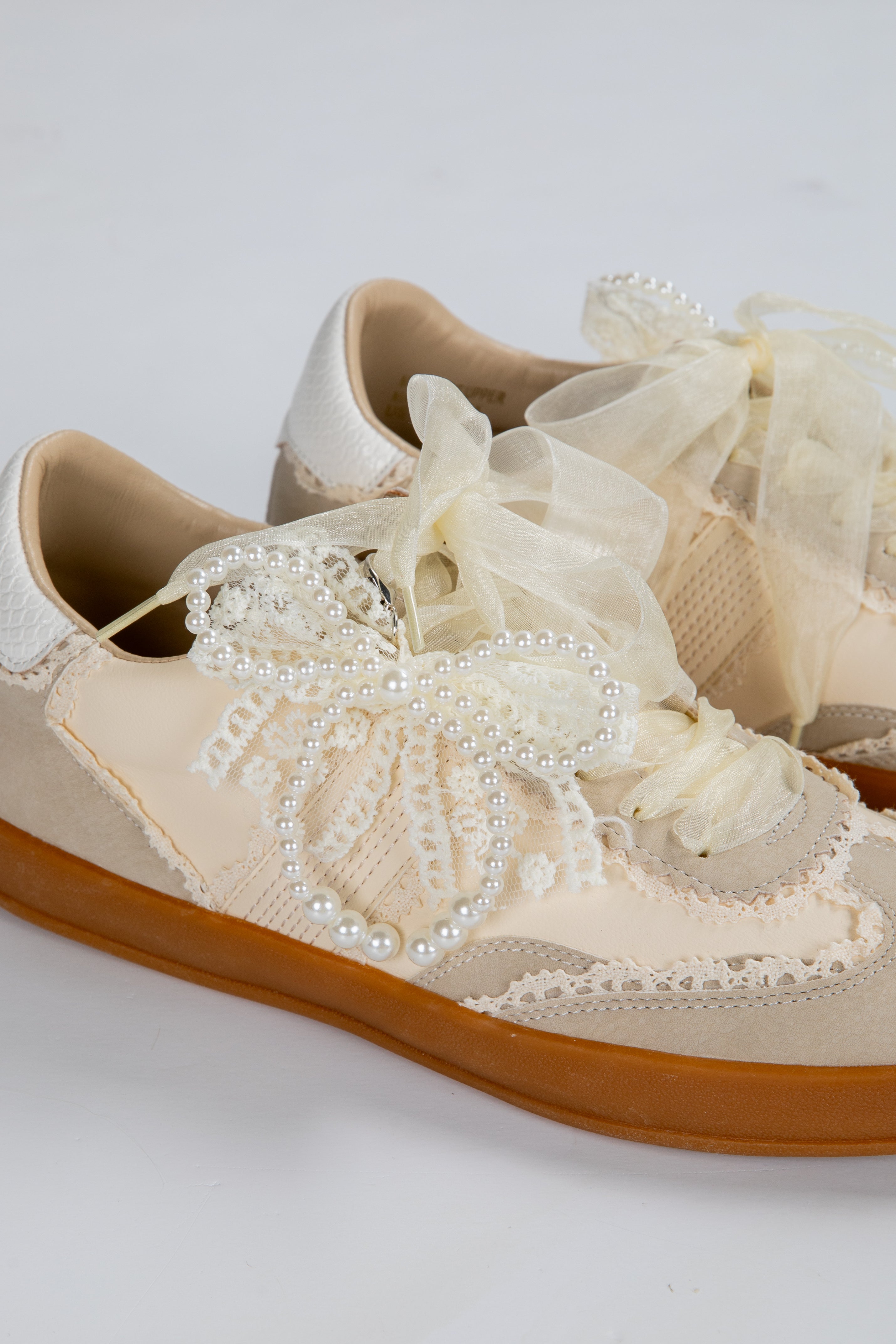 Beige lace-up shoe with decorative elements on a light gray background