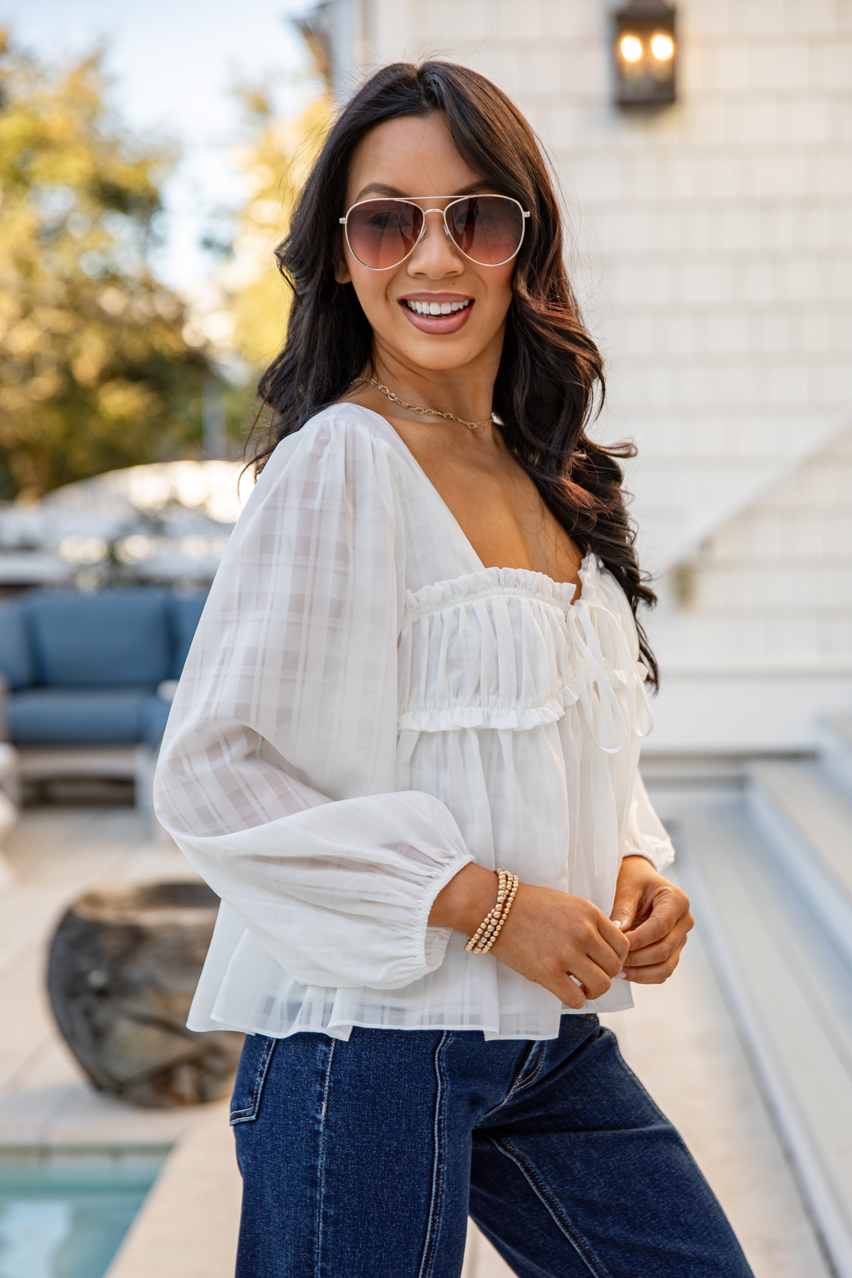 Woman wearing a white blouse and blue jeans outdoors.