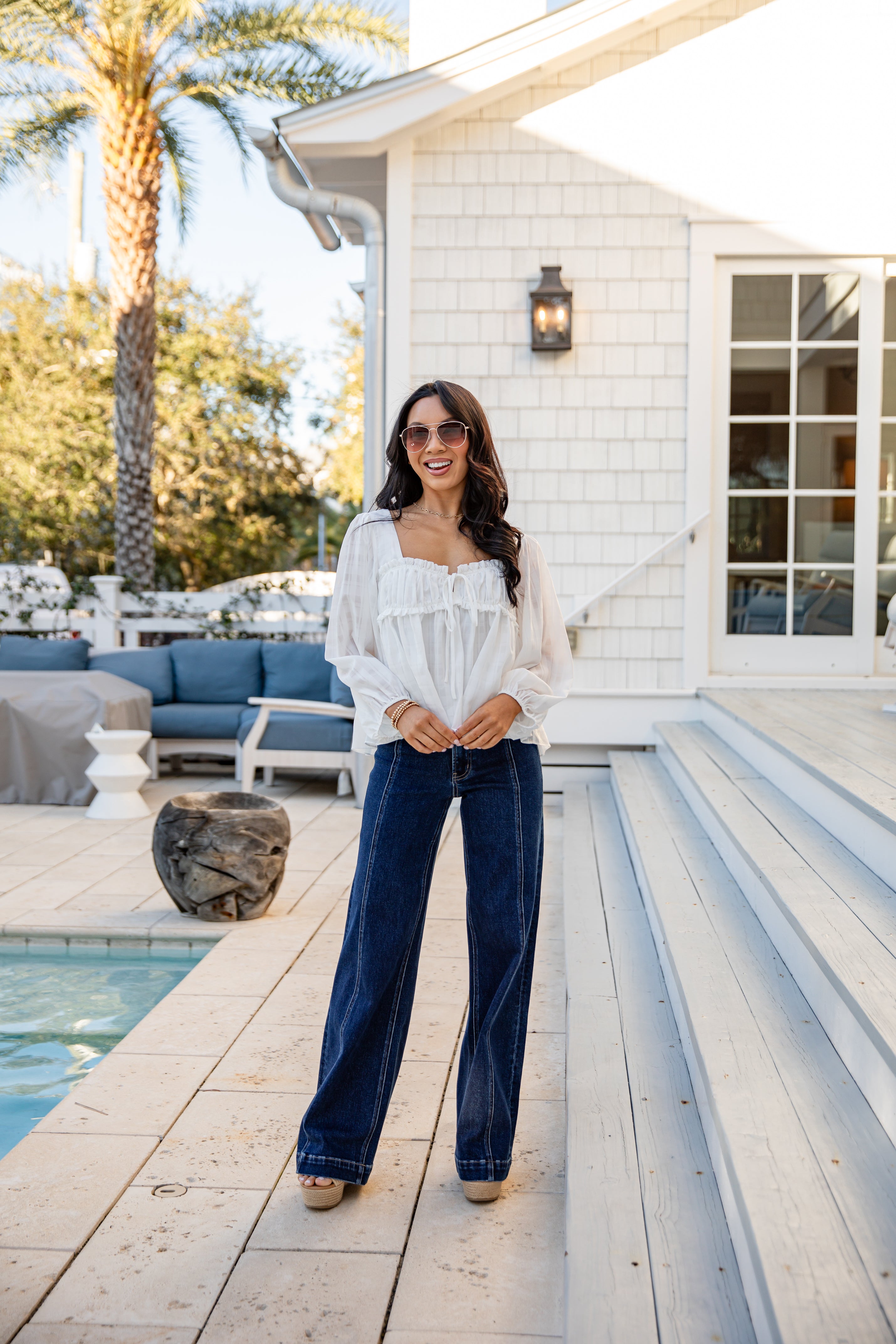 Woman standing by a poolside with a house and palm tree in the background