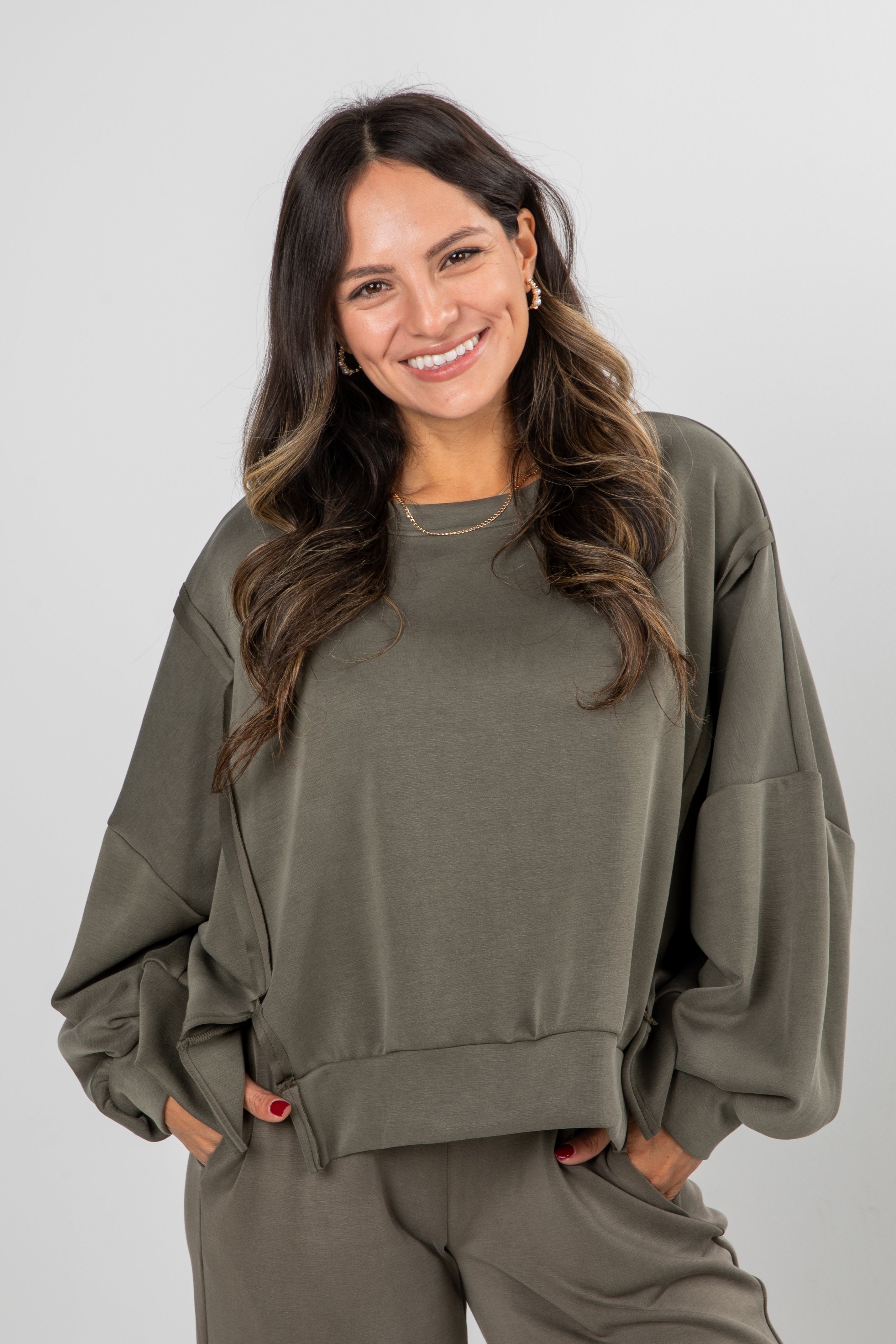 Woman wearing an olive green sweatshirt and pants on a plain background