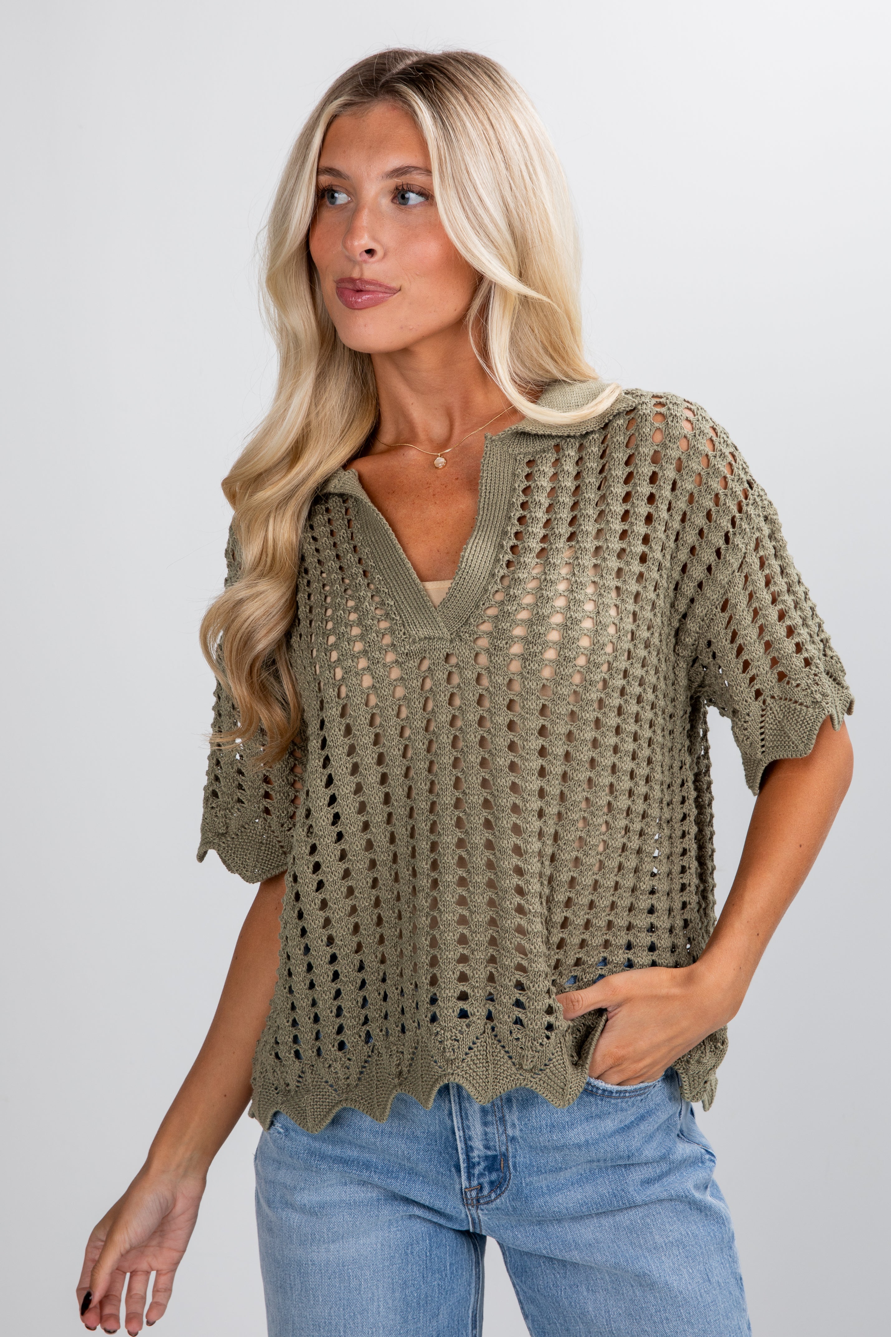 Woman wearing a green crochet top and blue jeans on a plain background