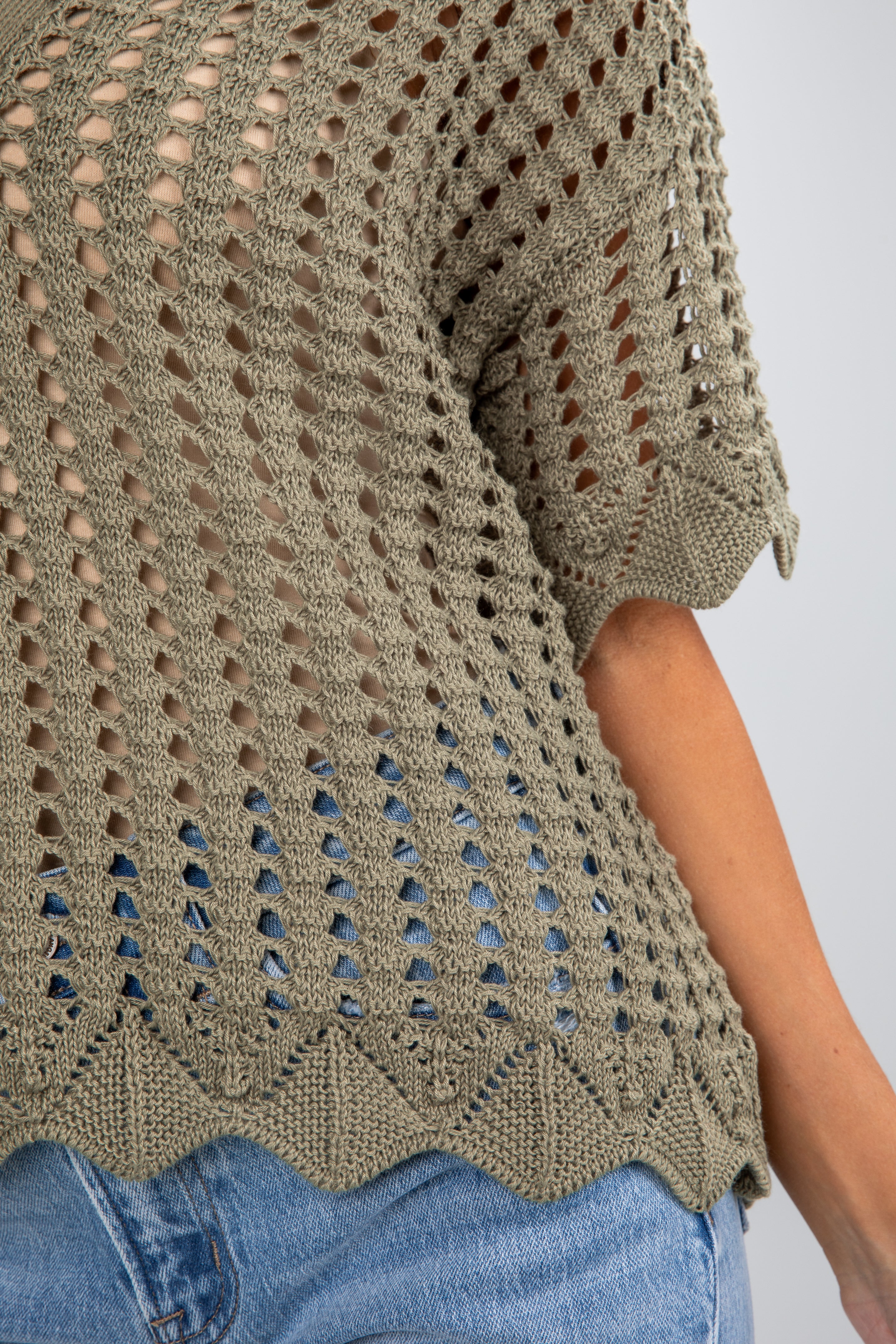 Close-up of a person wearing a green crochet top with a white background