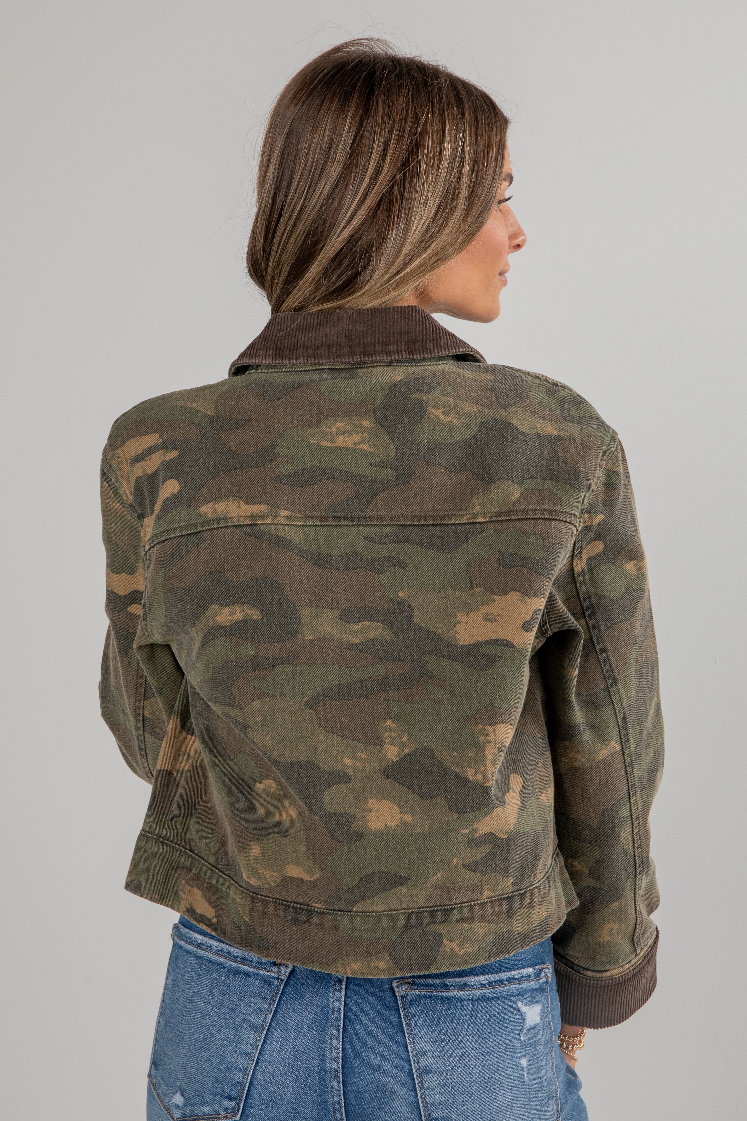 Person wearing a camouflage jacket and blue jeans on a gray background