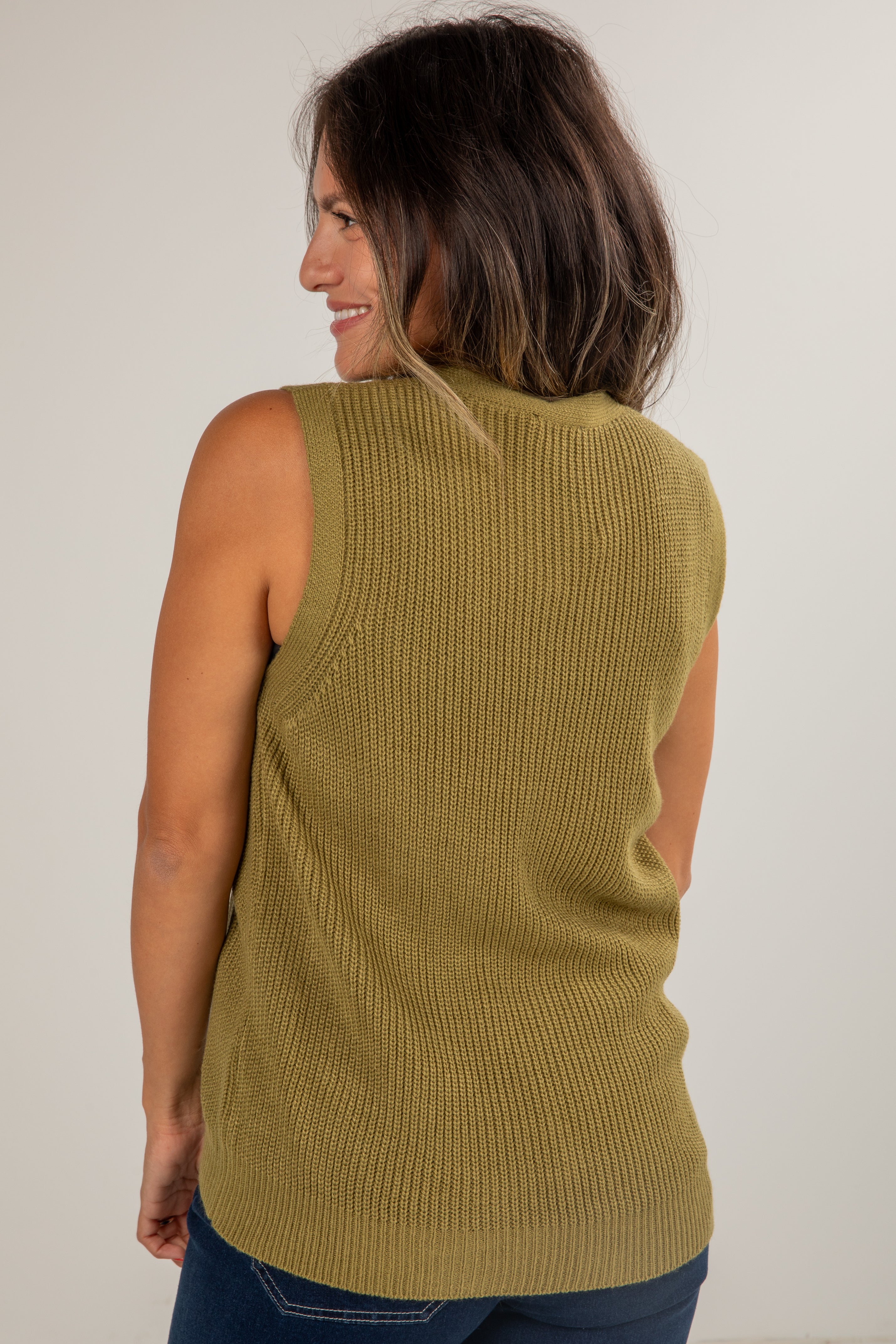 Woman wearing a green sleeveless knitted top against a plain background