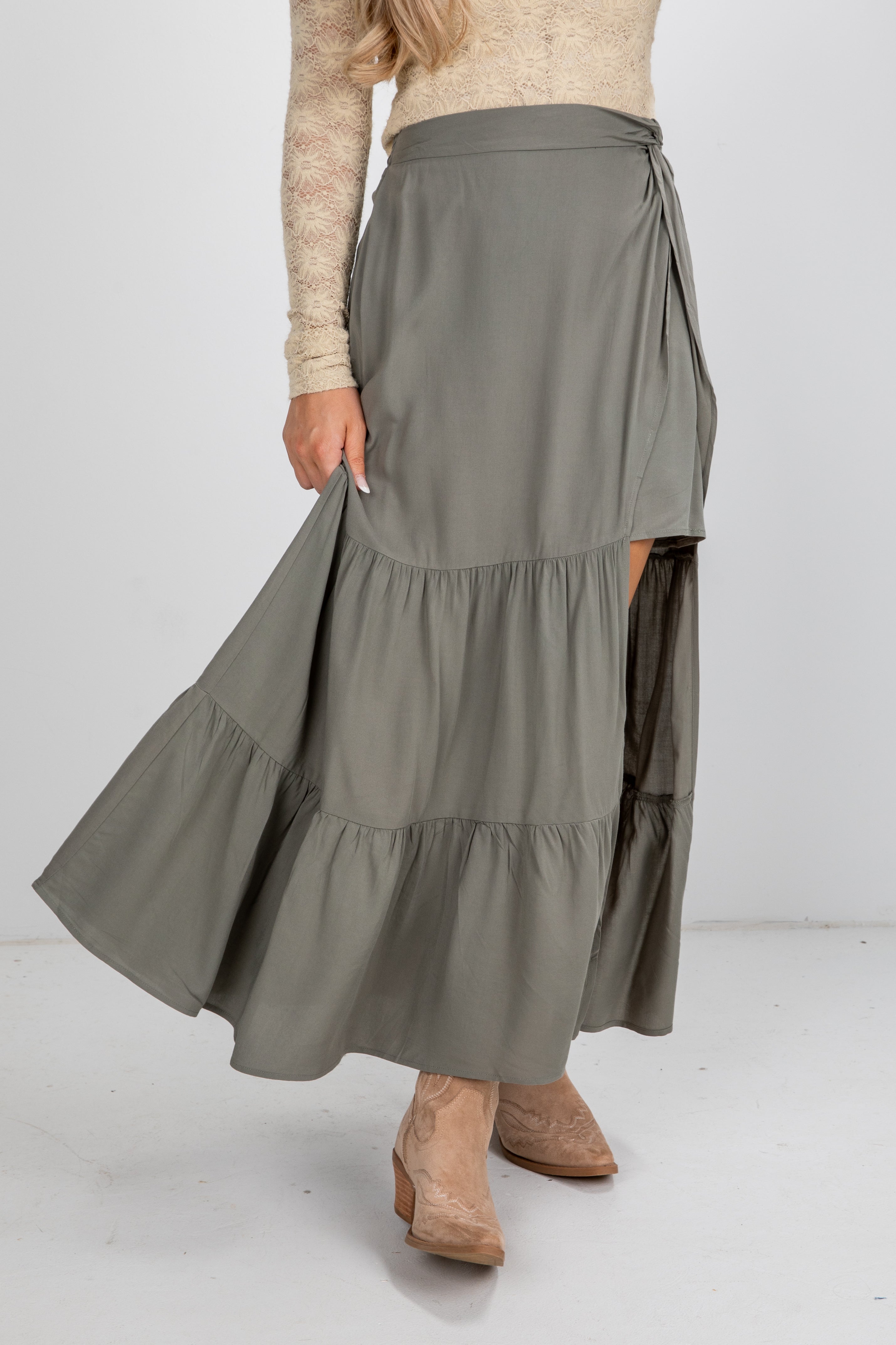 Person wearing a long olive green skirt with a plain background