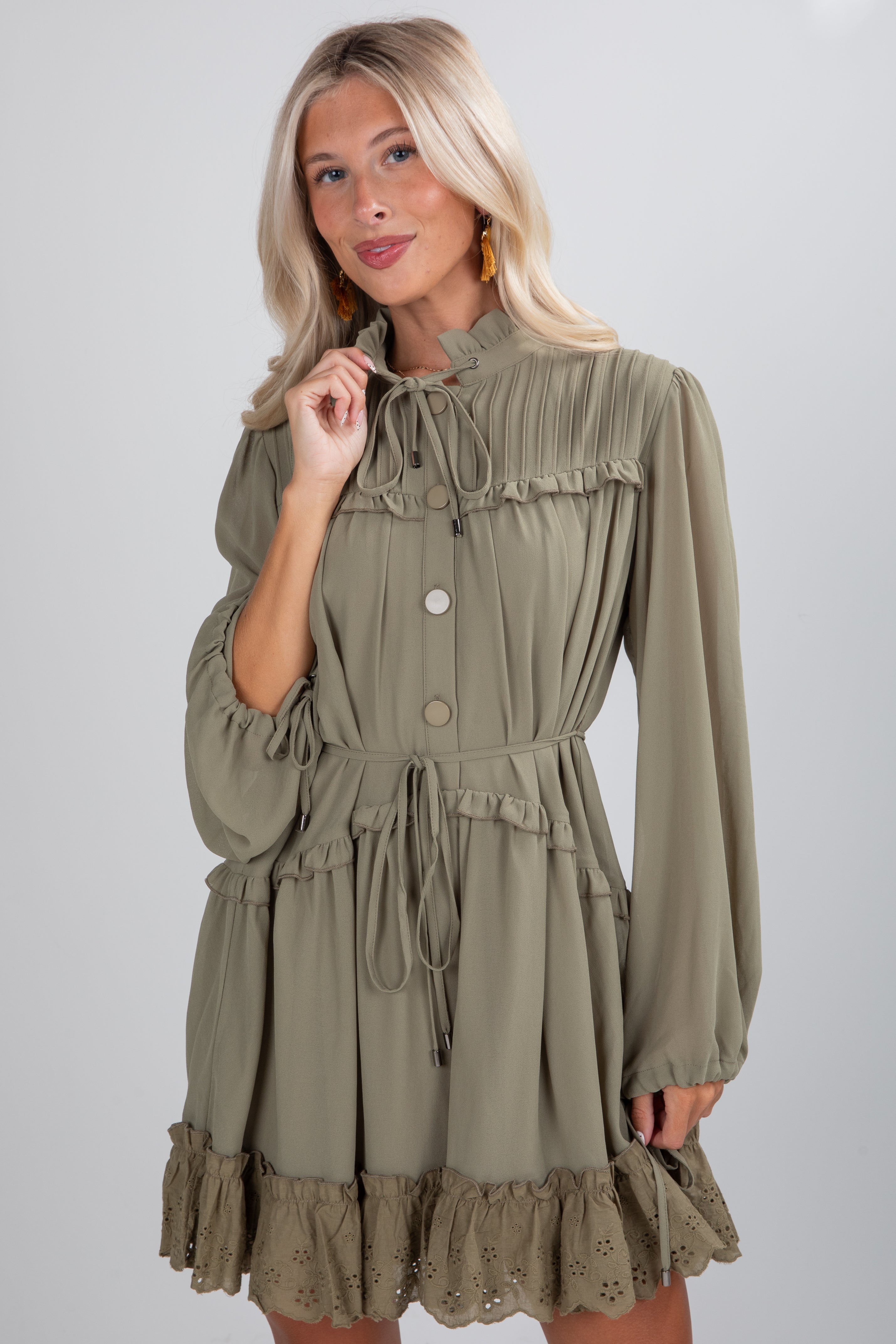 Woman wearing an olive green dress with long sleeves and ruffled details on a plain background