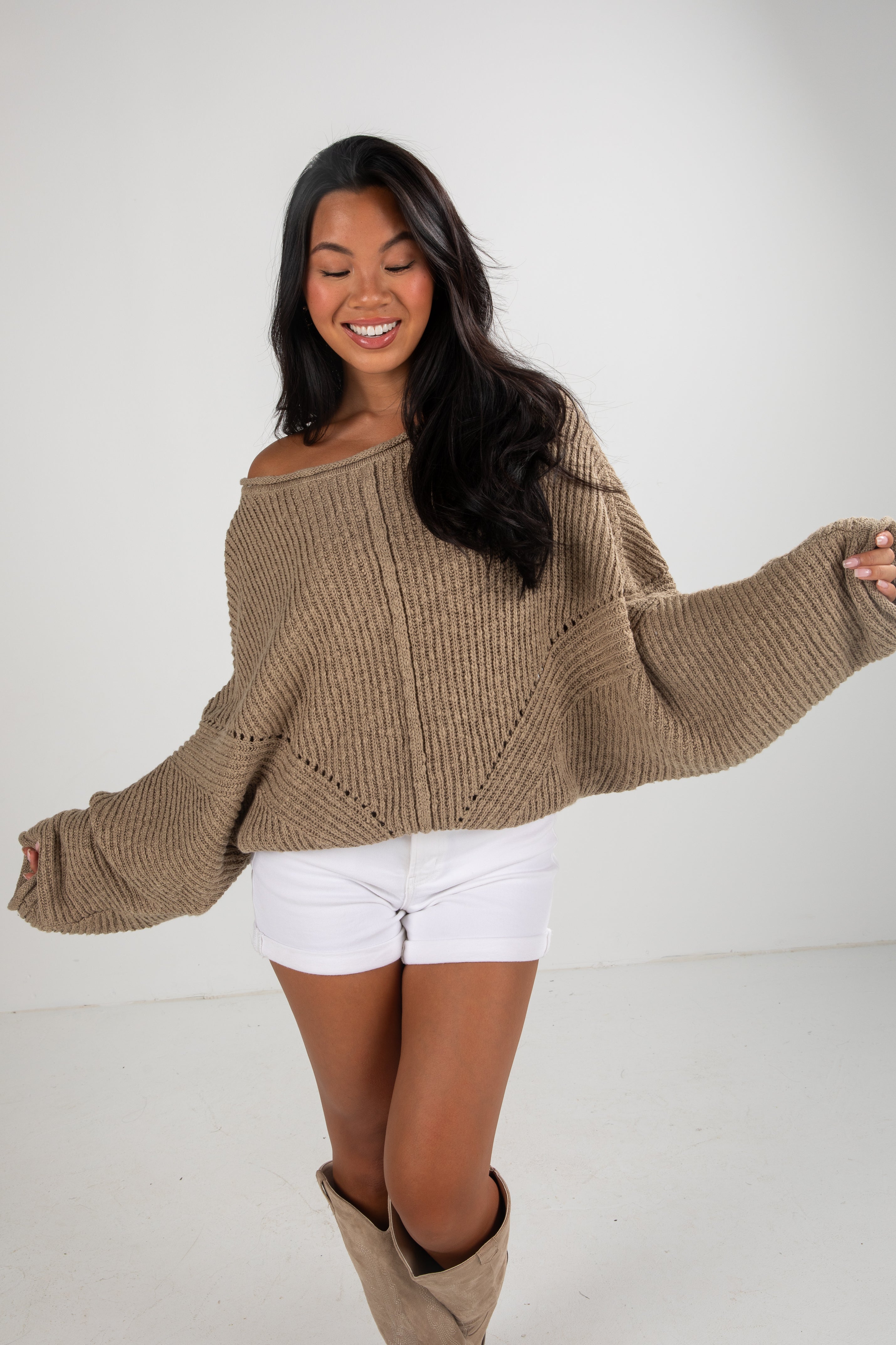 Woman wearing a beige sweater and white shorts on a white background