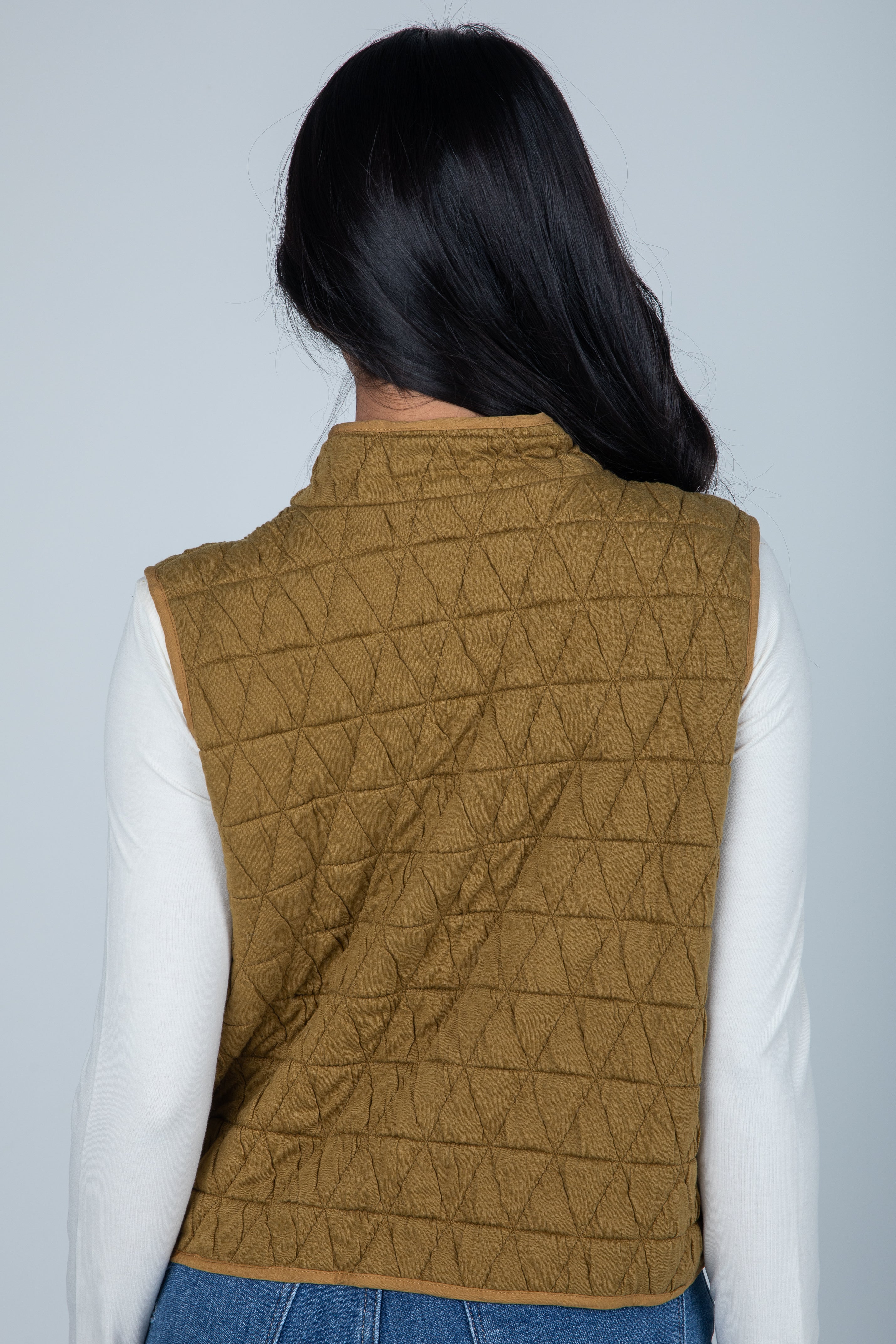 Person wearing a quilted brown vest against a light gray background