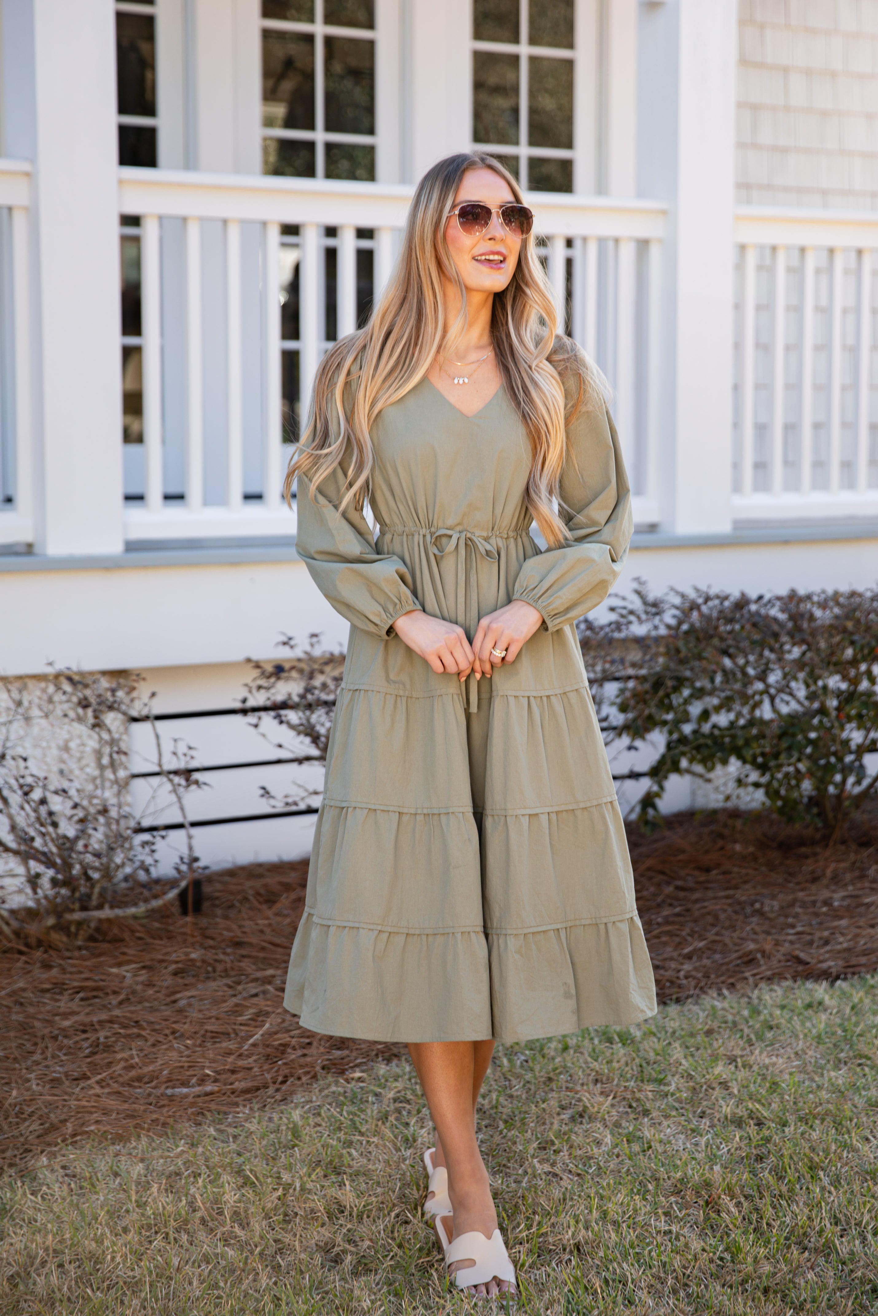 Woman wearing a green dress standing in front of a white house with a porch.