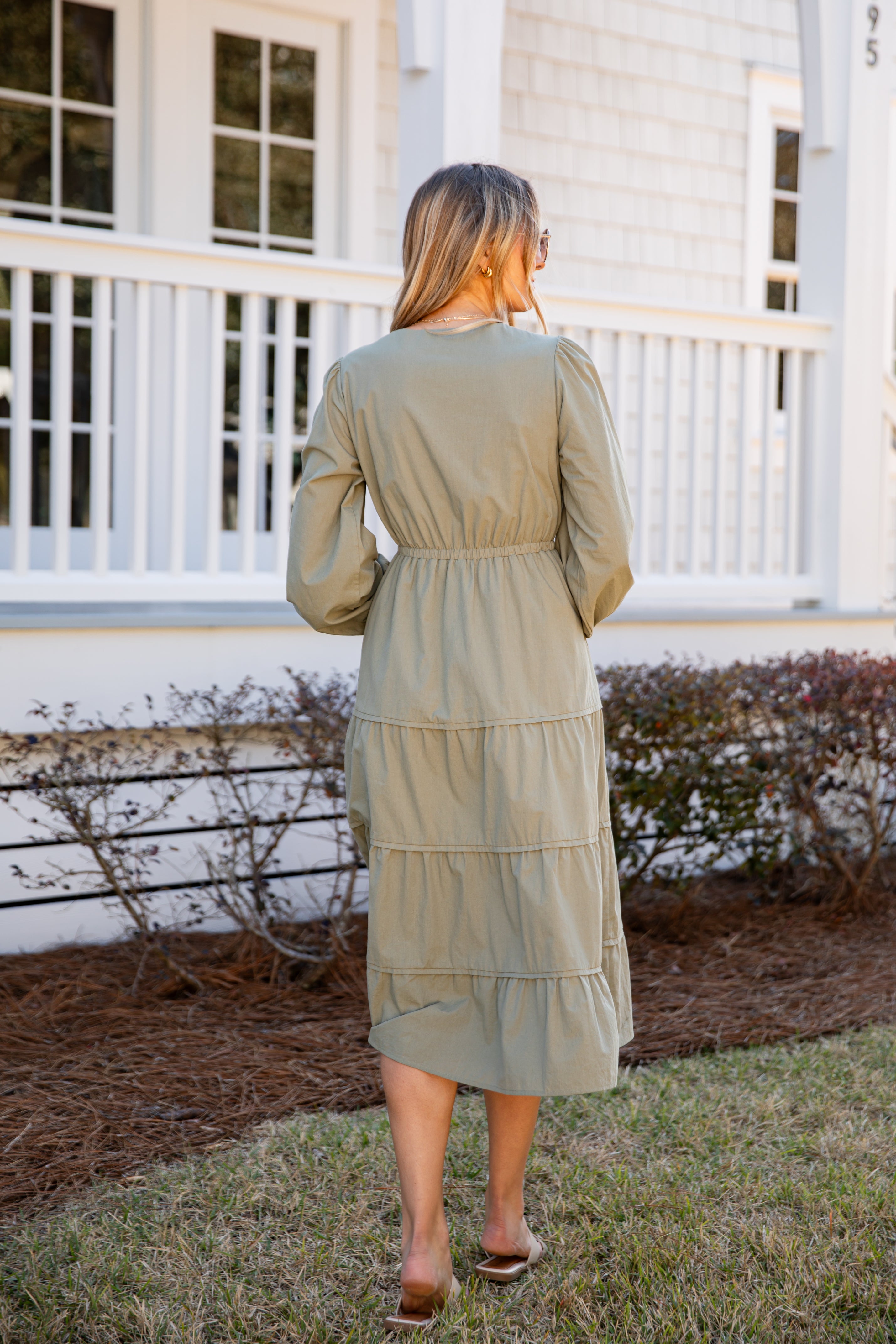 Woman wearing a green dress standing on a grassy area with a white house in the background.