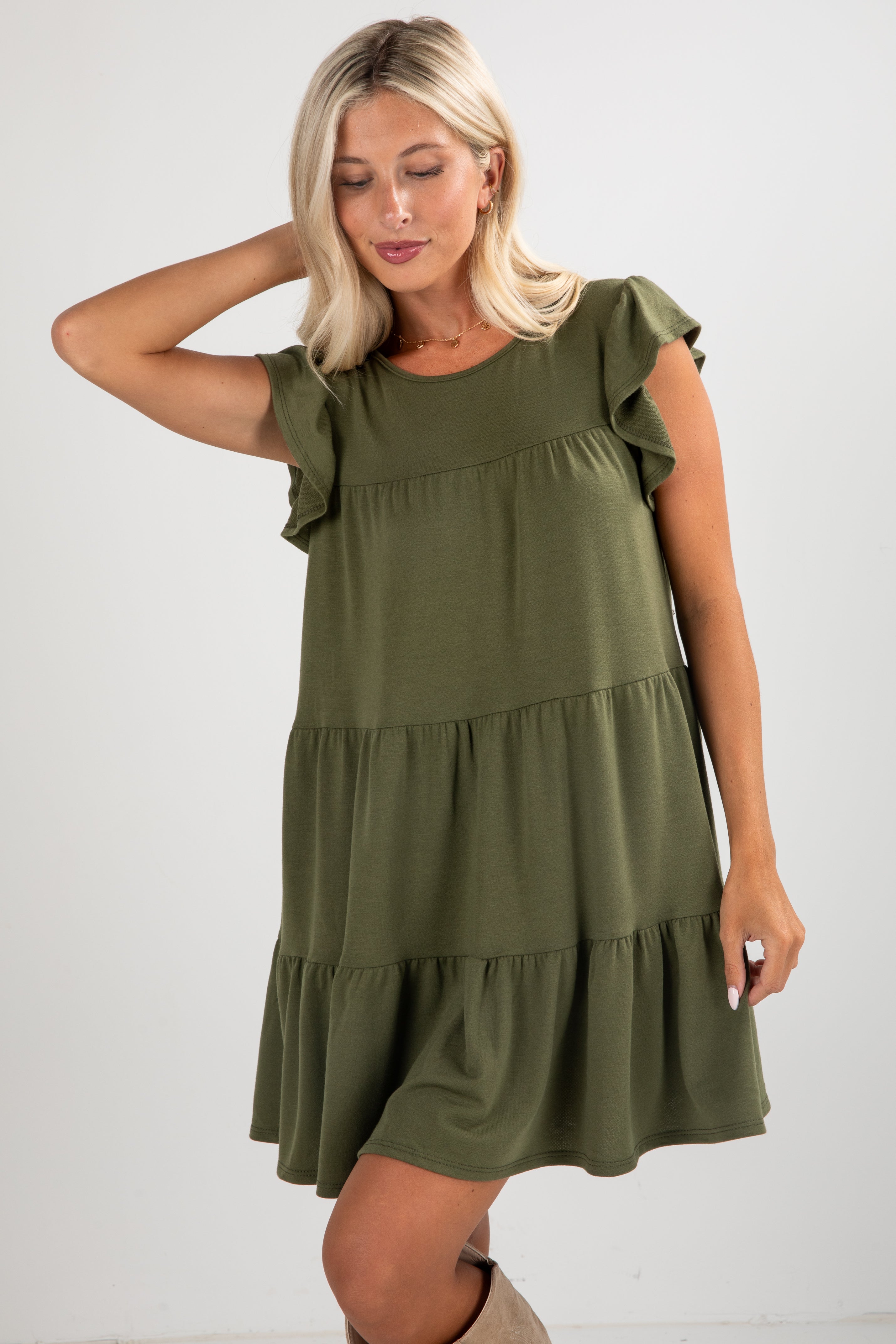 Woman wearing an olive green dress with ruffled sleeves and layers on a white background