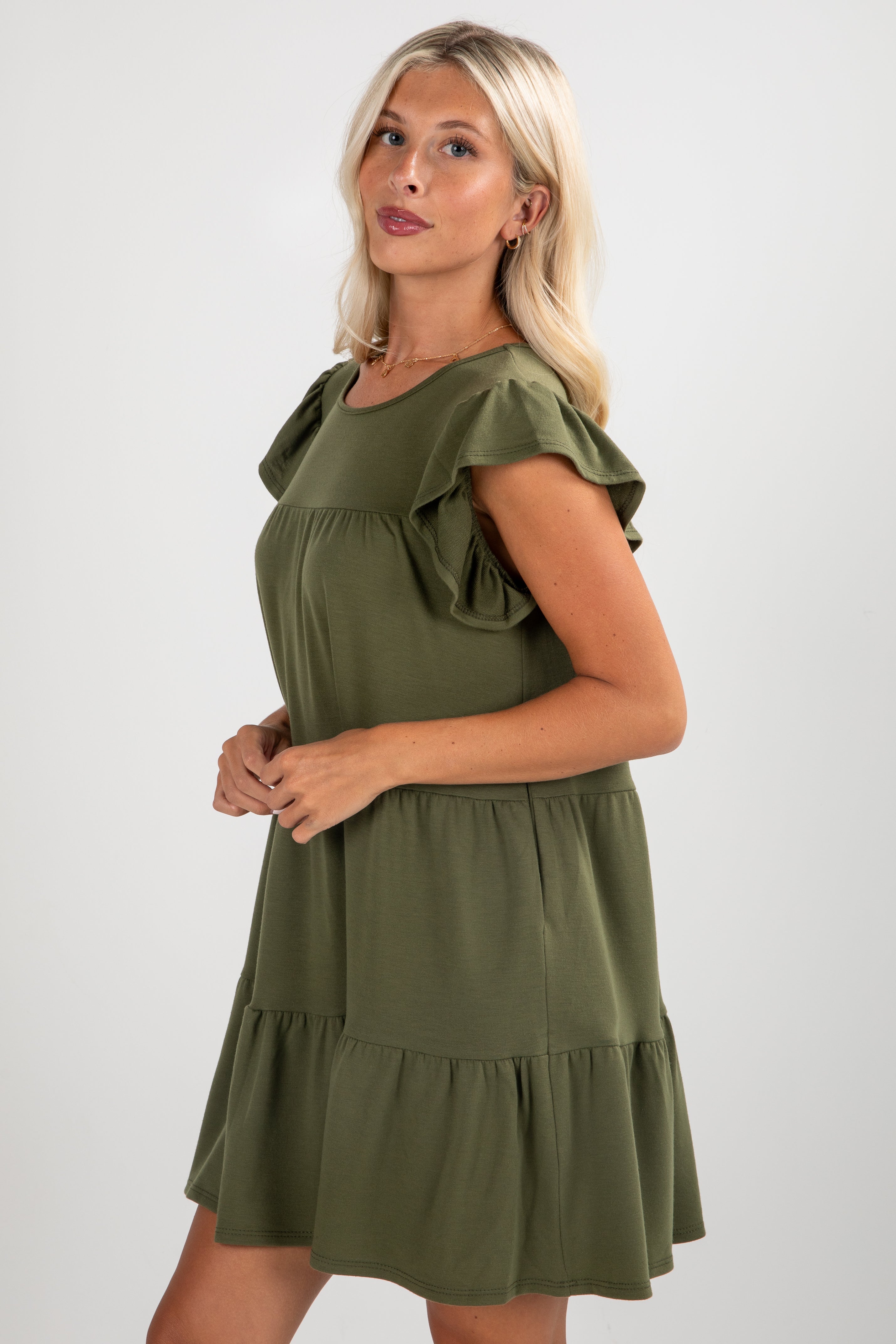 Woman wearing an olive green dress with ruffled sleeves on a white background