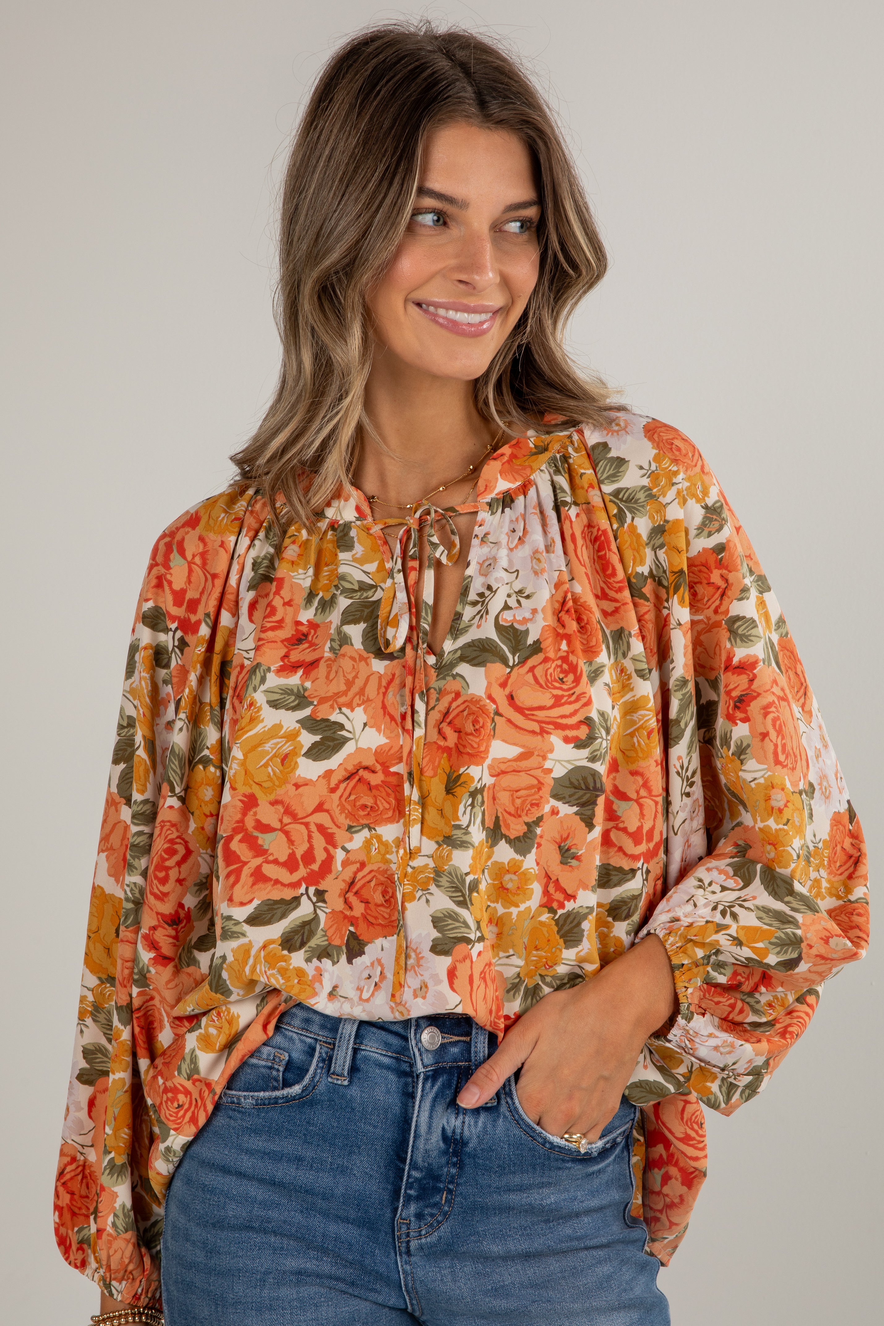 Woman wearing a floral blouse with long sleeves and blue jeans on a plain background