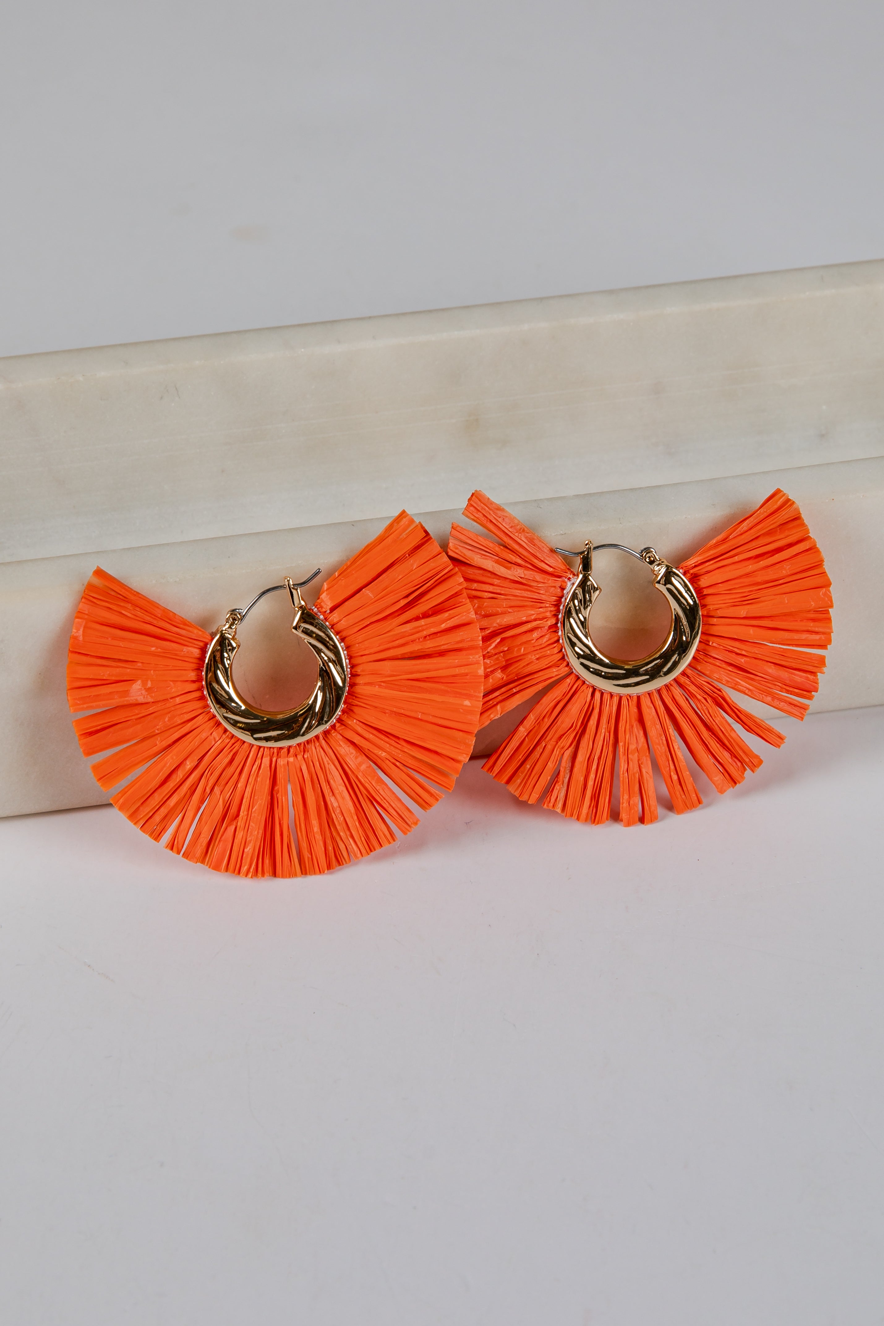 Orange ruffled earrings with gold hoop centers on a light background