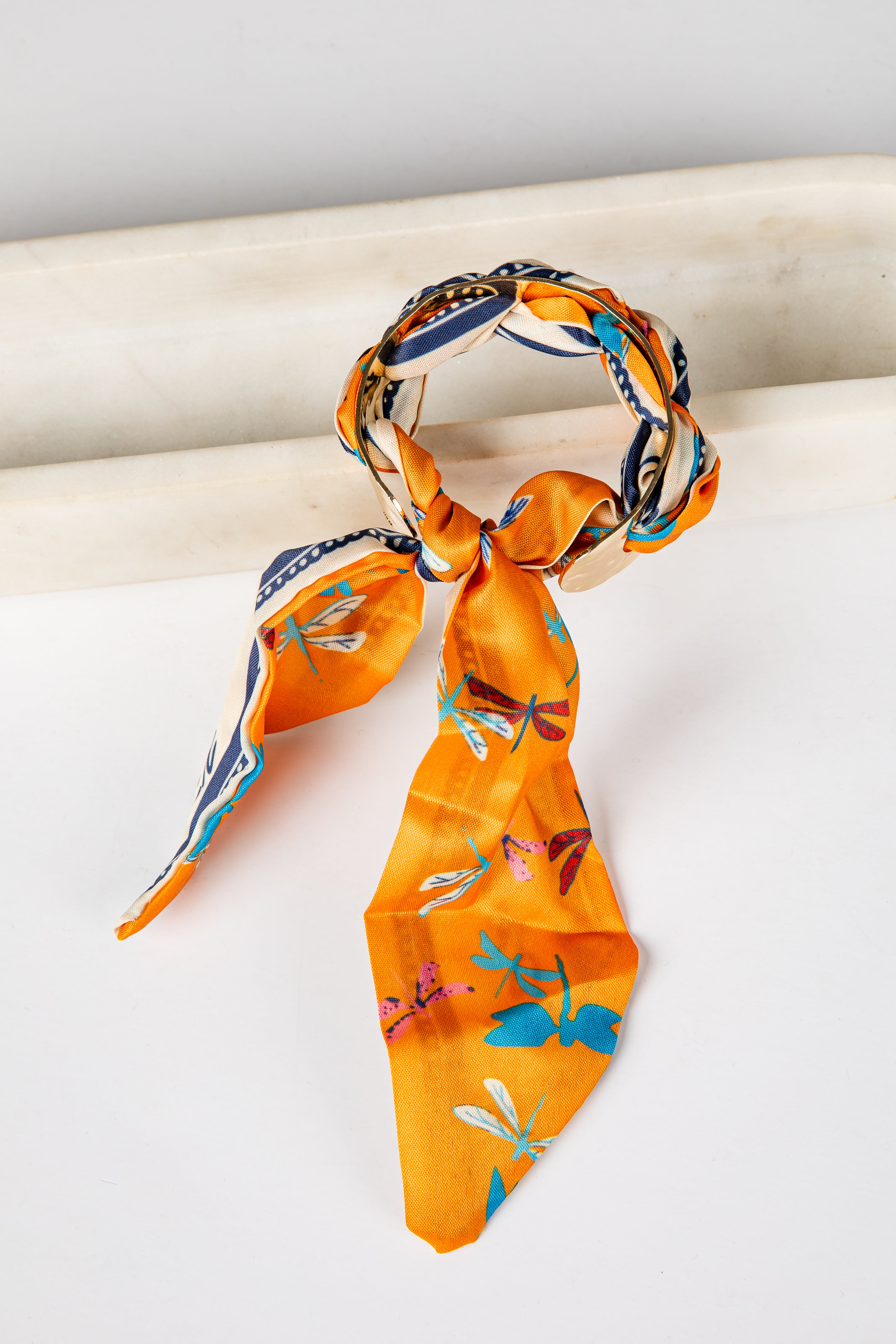 Orange scarf bracelet with dragonfly pattern tied around a white surface
