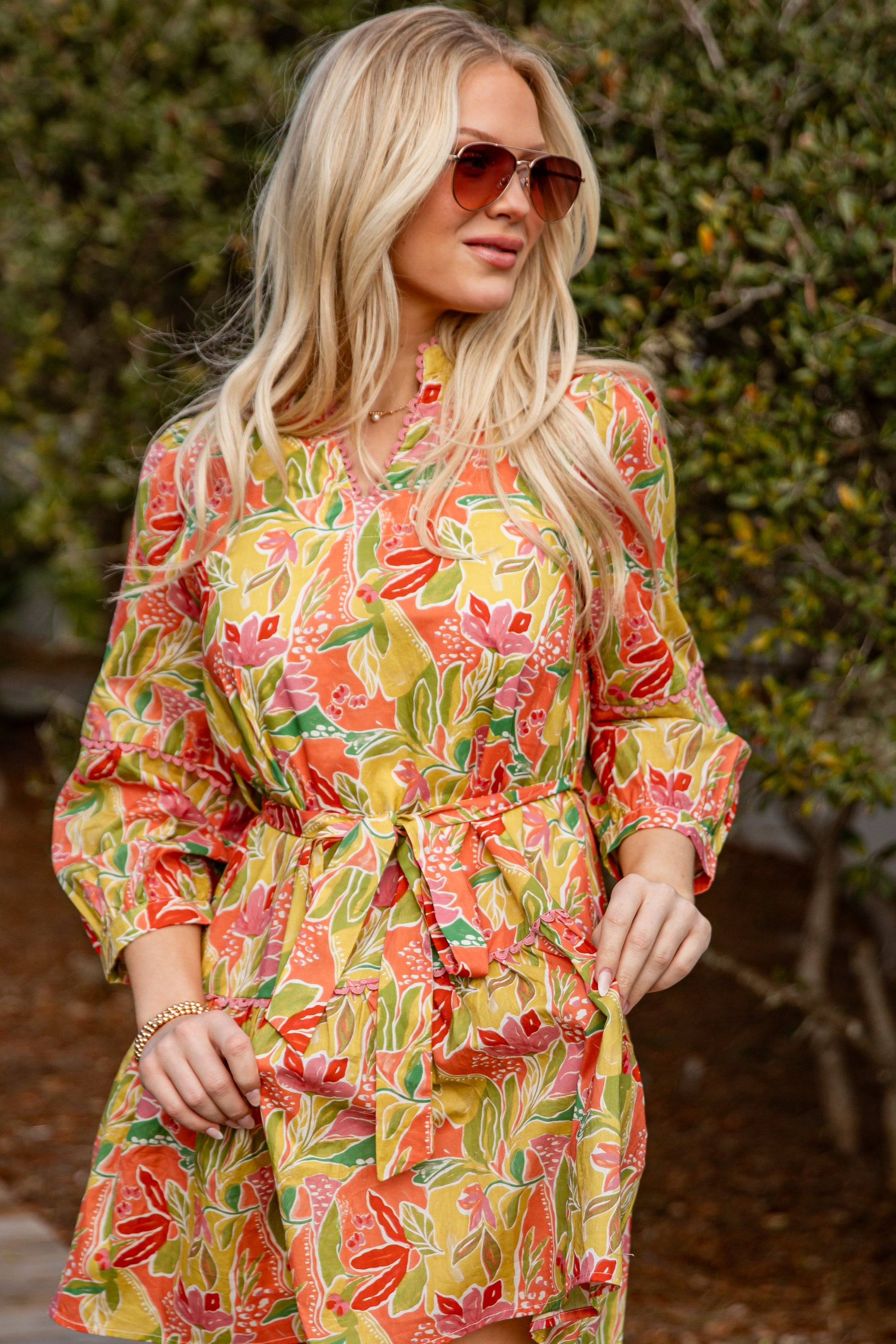 Woman wearing a colorful floral dress and sunglasses outdoors.