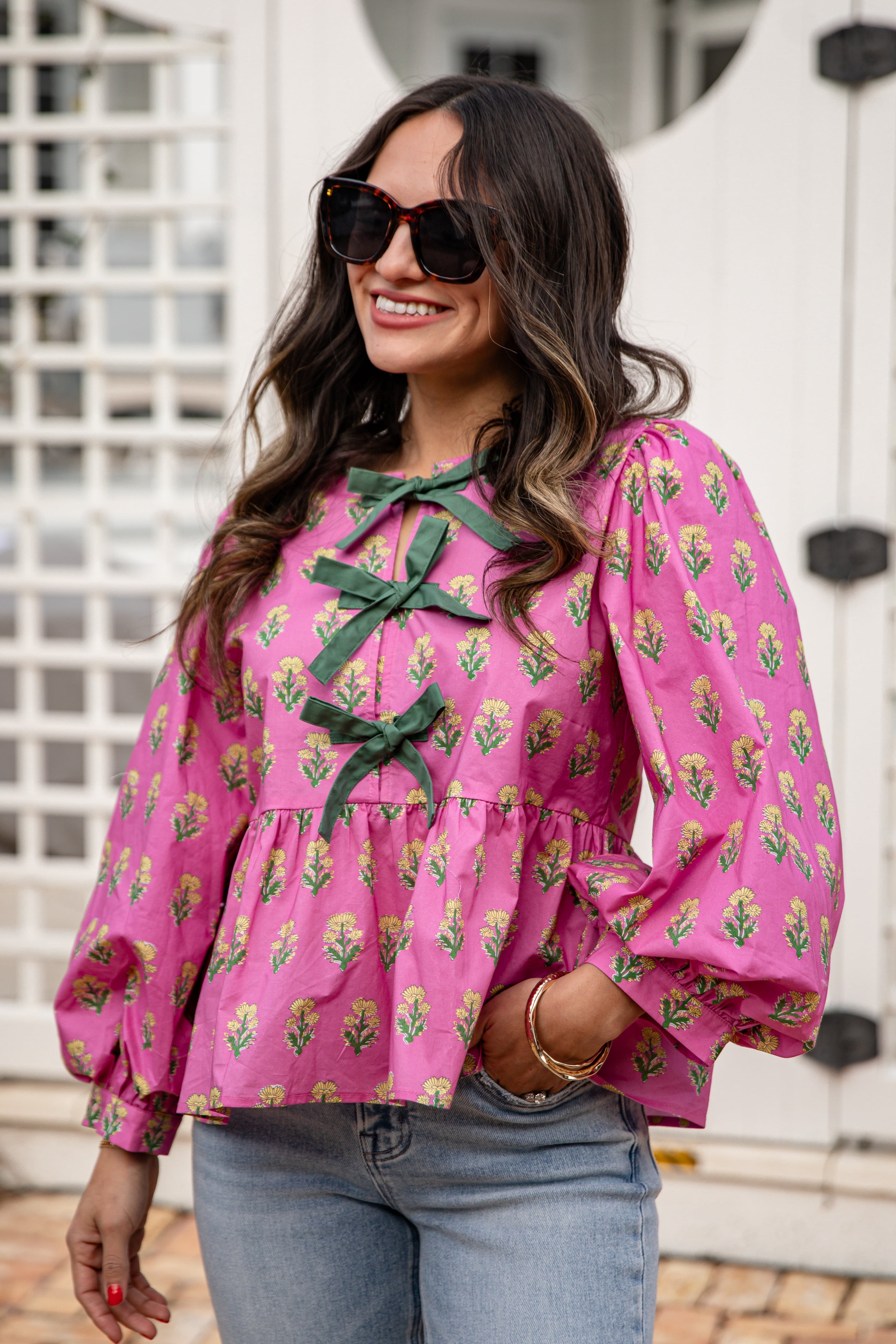 Woman wearing a pink floral blouse with green ribbons in an outdoor setting
