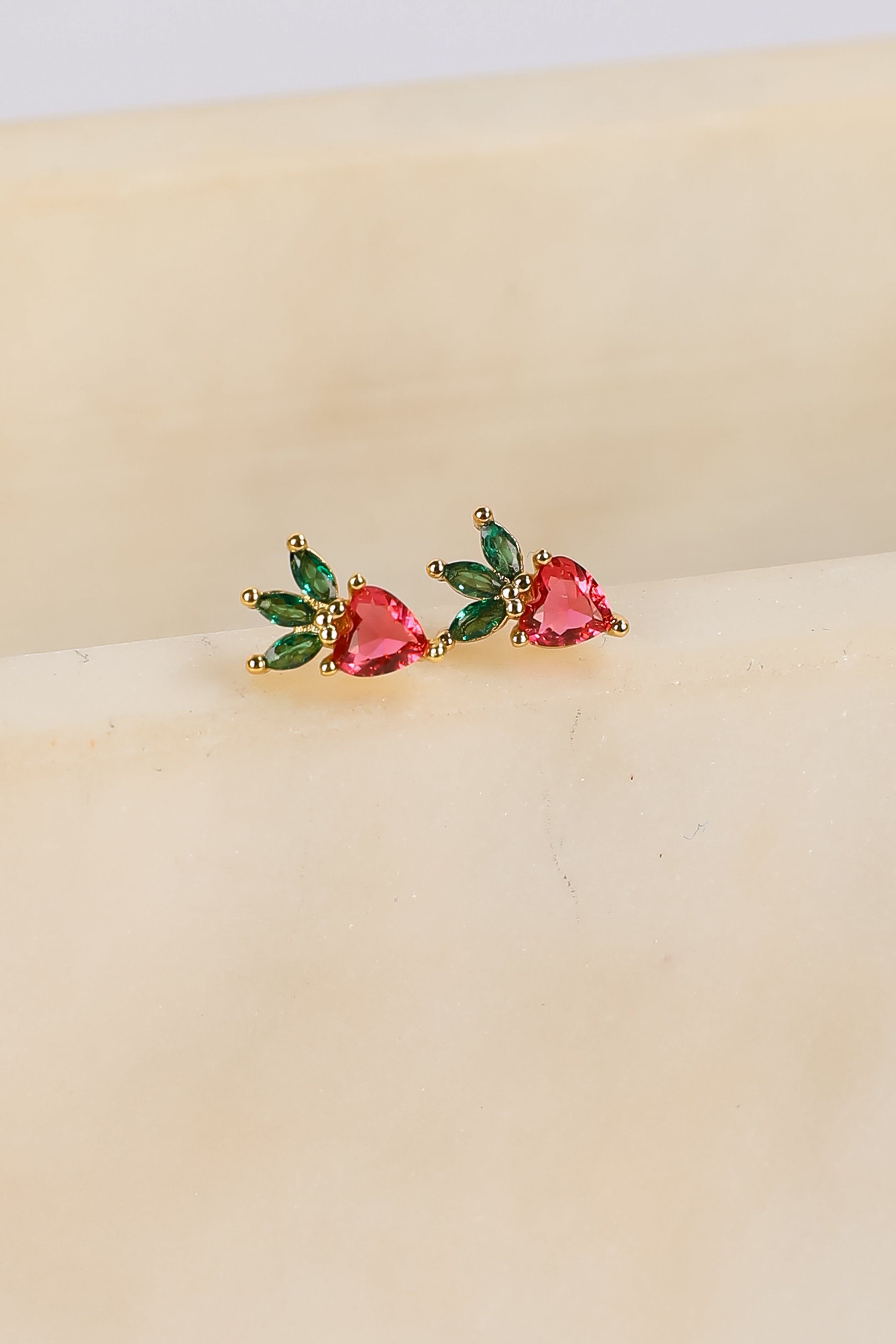 Pair of earrings with heart-shaped gemstones on a beige surface