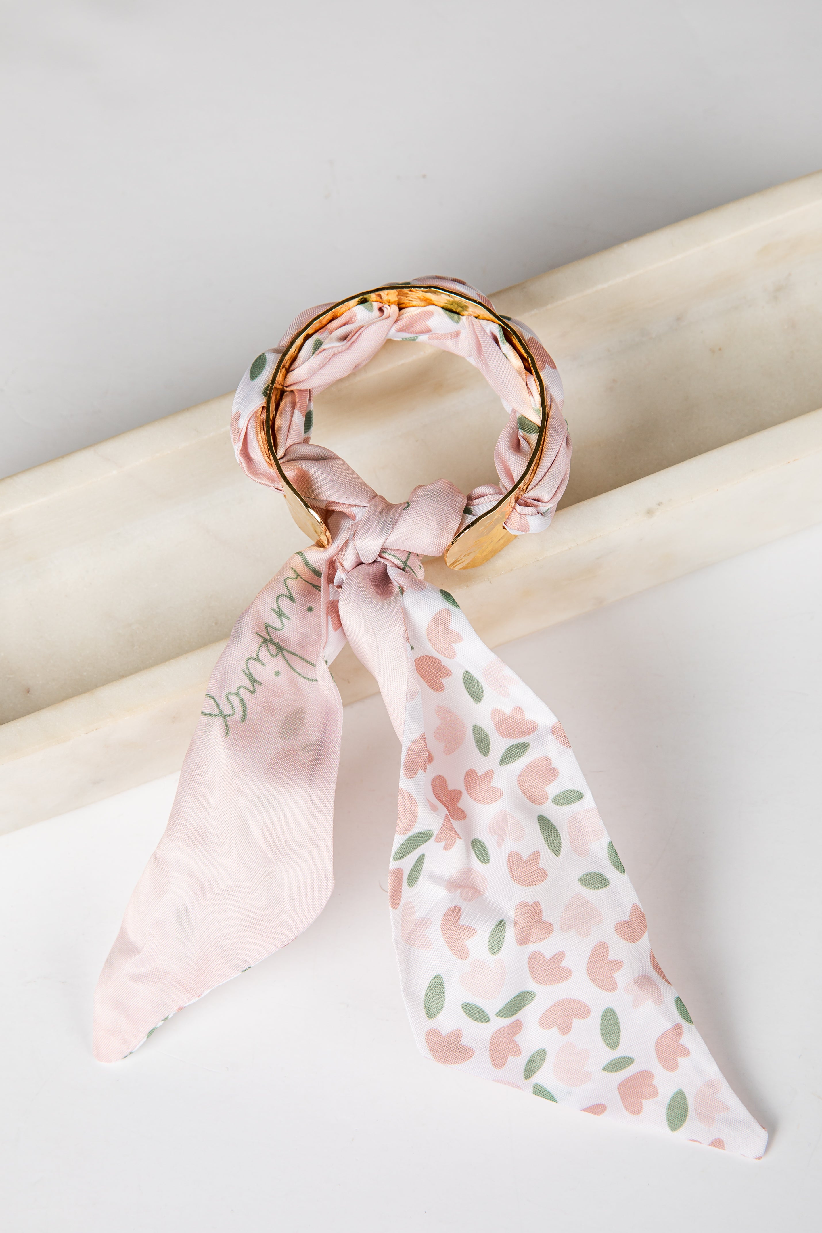 Pink floral bracelet scarf on a wooden stick against a light background