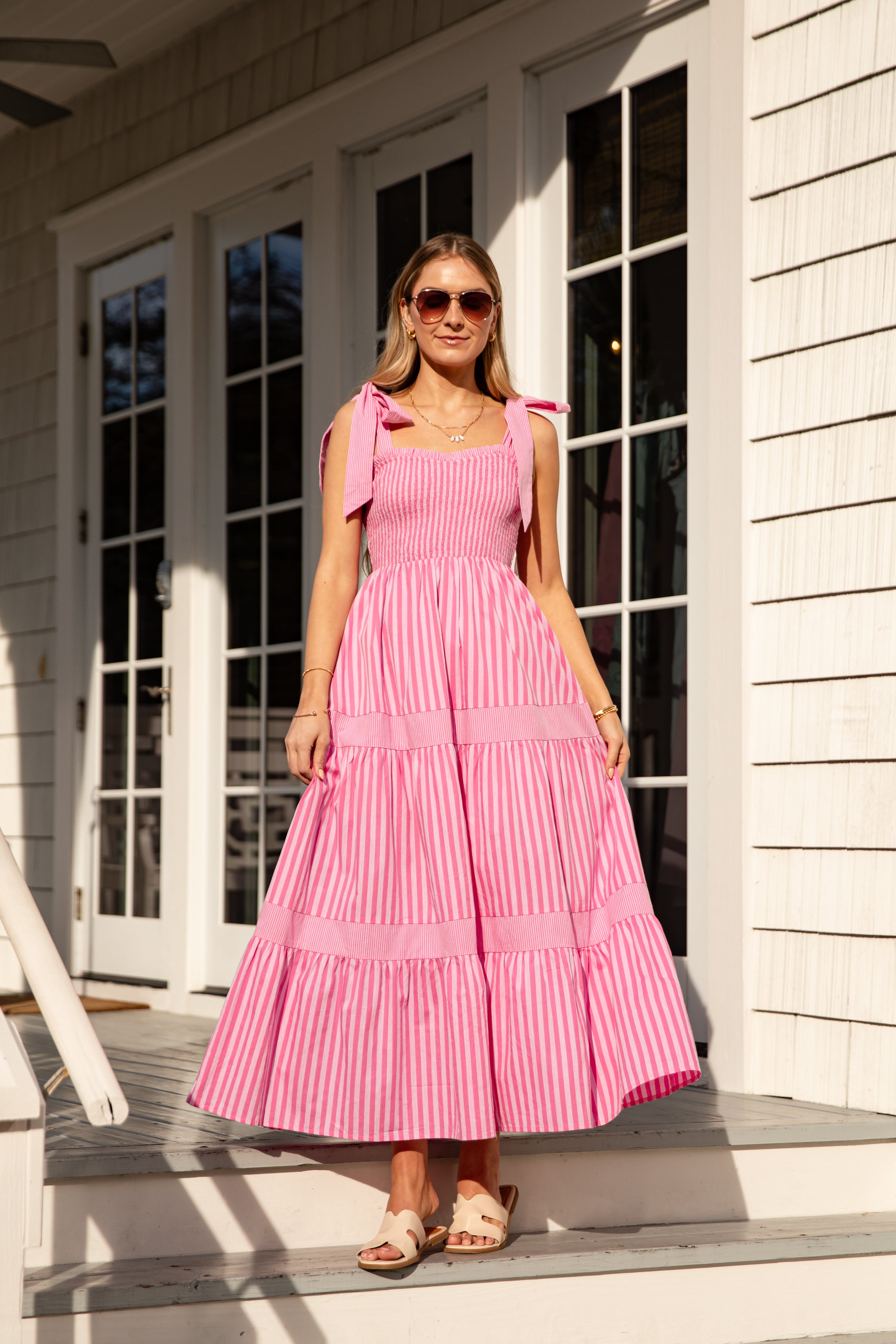 Woman wearing a pink dress standing on a porch.