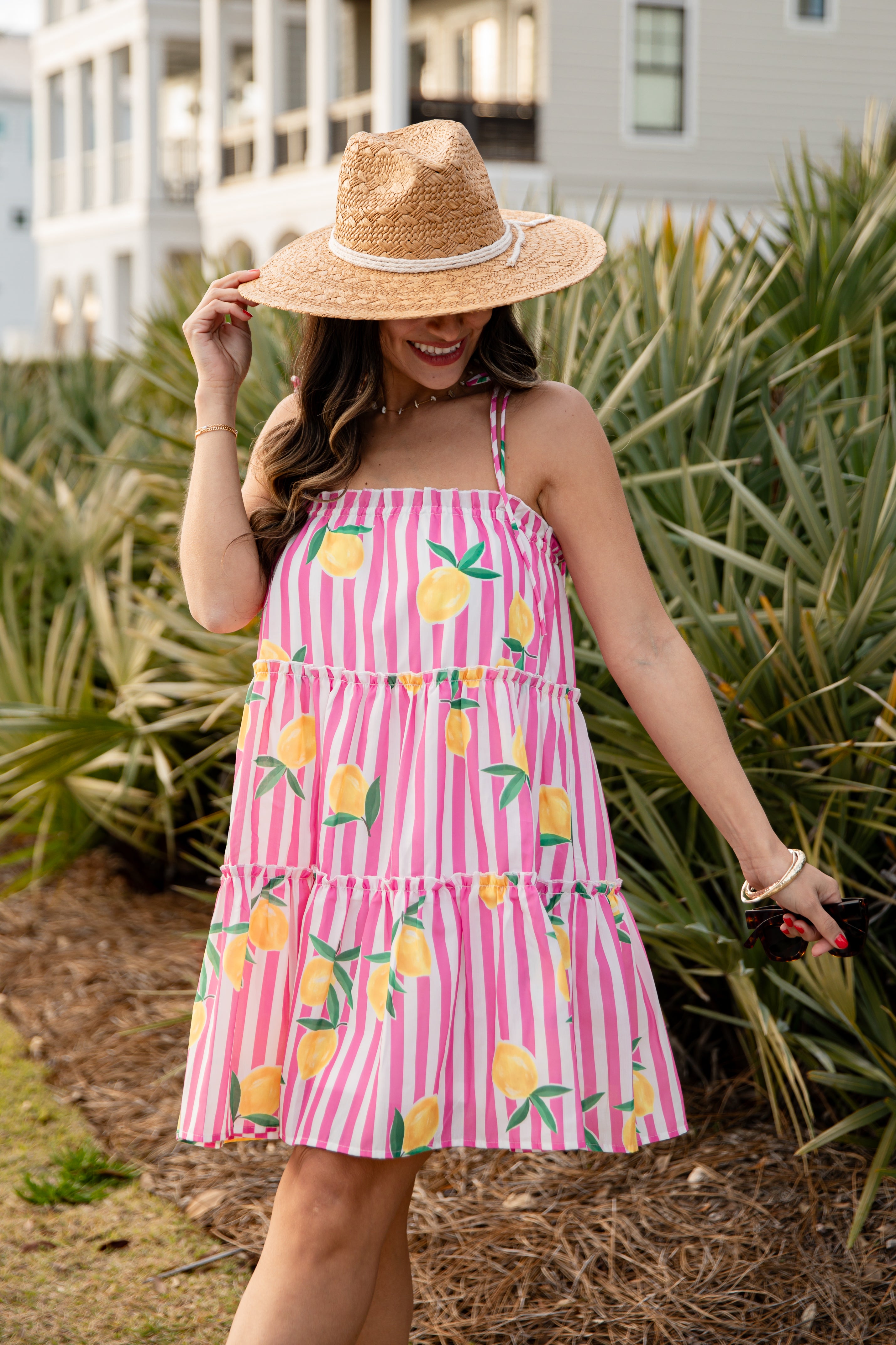 Woman wearing a pink dress with lemon print and a straw hat in a garden setting