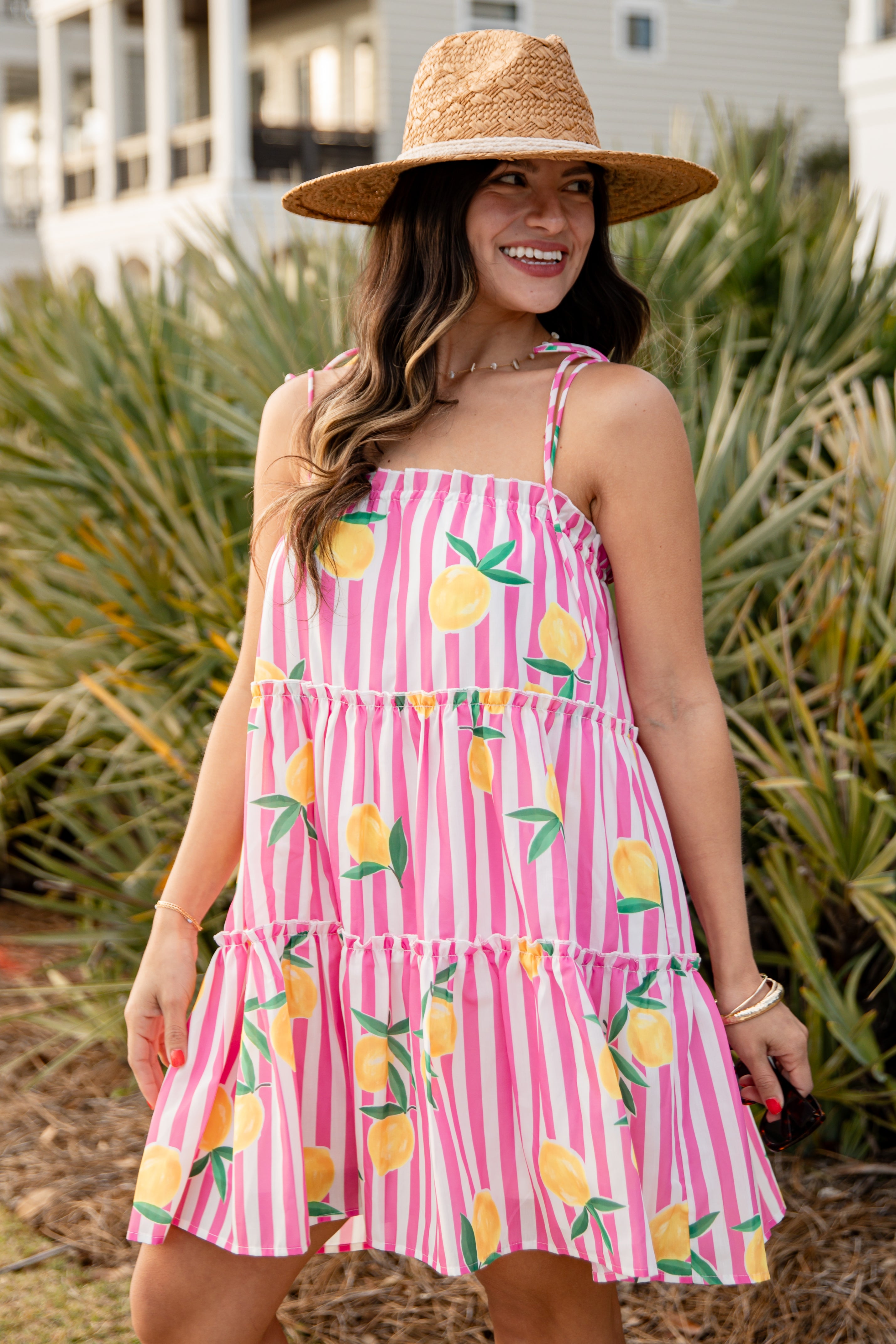 Woman wearing a pink striped dress with lemon print and a straw hat outdoors.