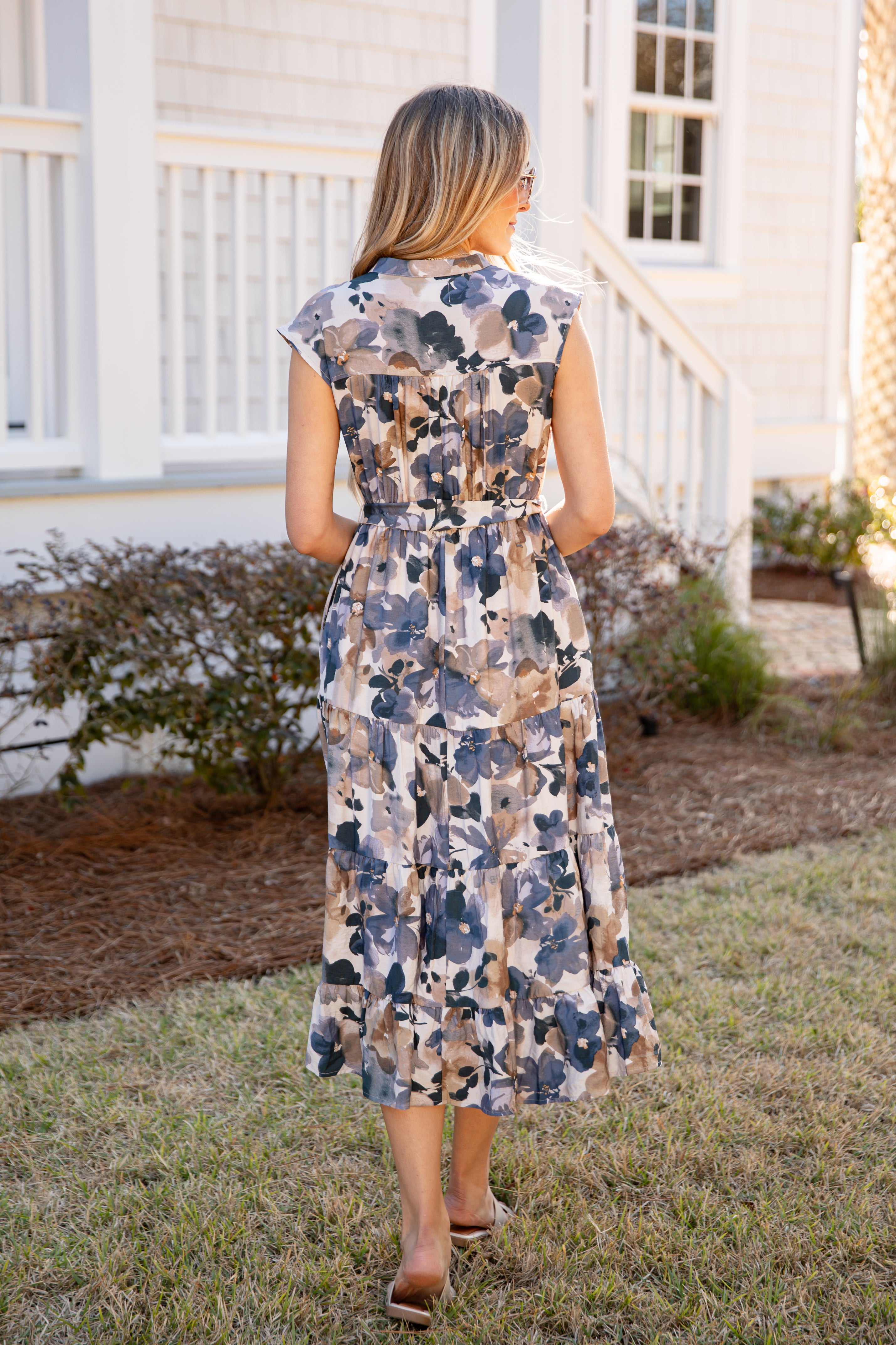 Woman wearing a floral dress standing in front of a house.