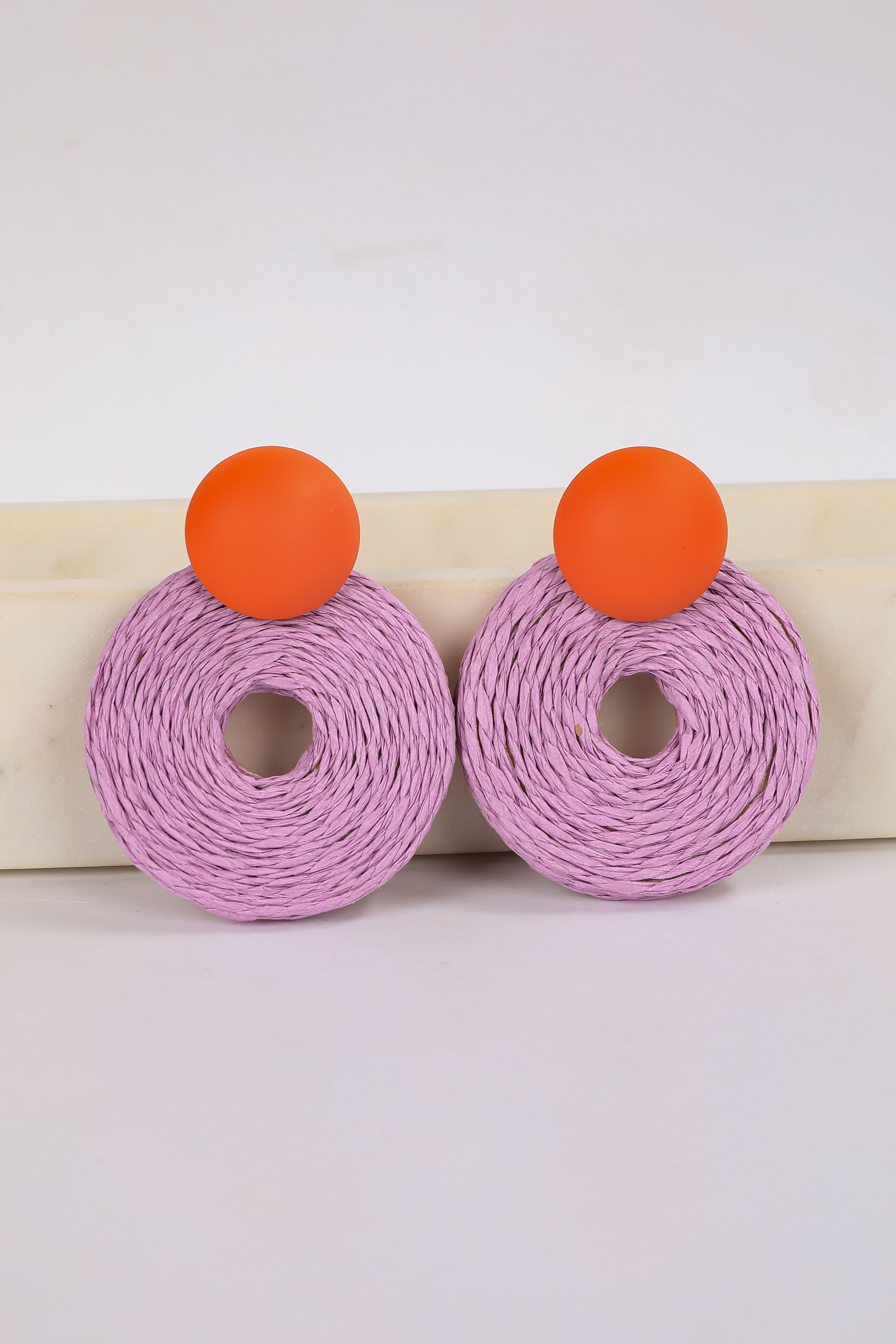 Pair of earrings with purple circular design and orange accents on a white background