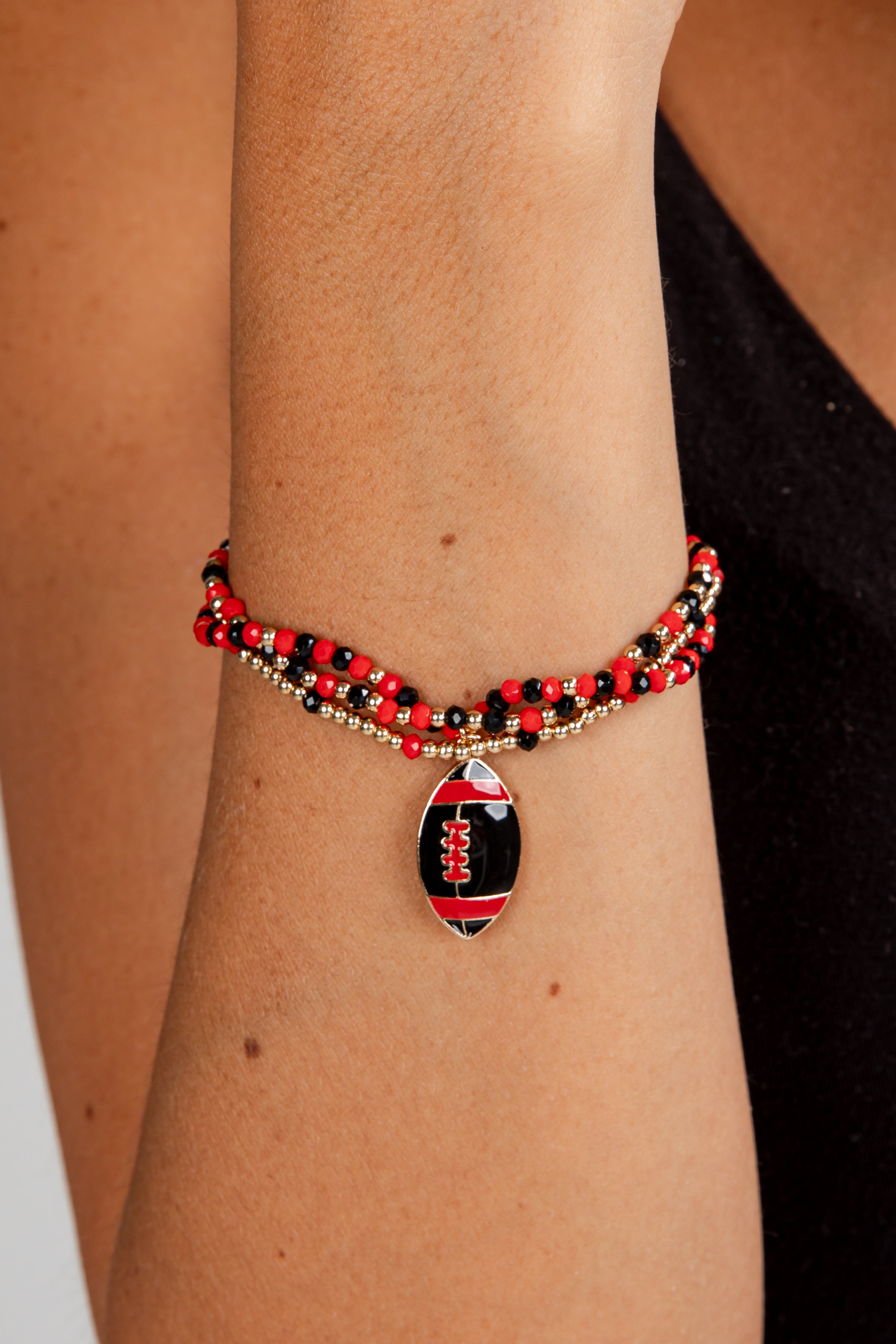 Bracelet with football charm on a wrist against a neutral background