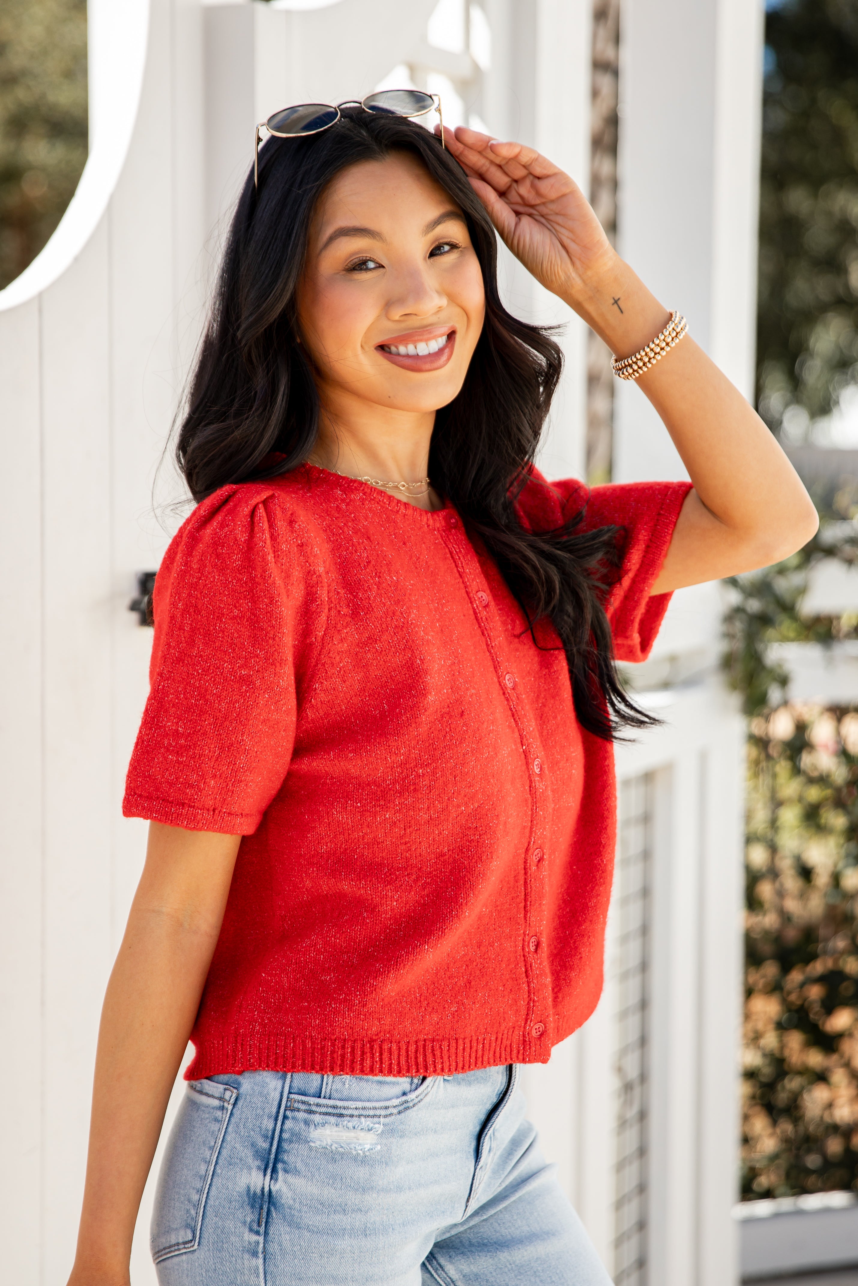Woman wearing a red top and blue jeans, standing outdoors.