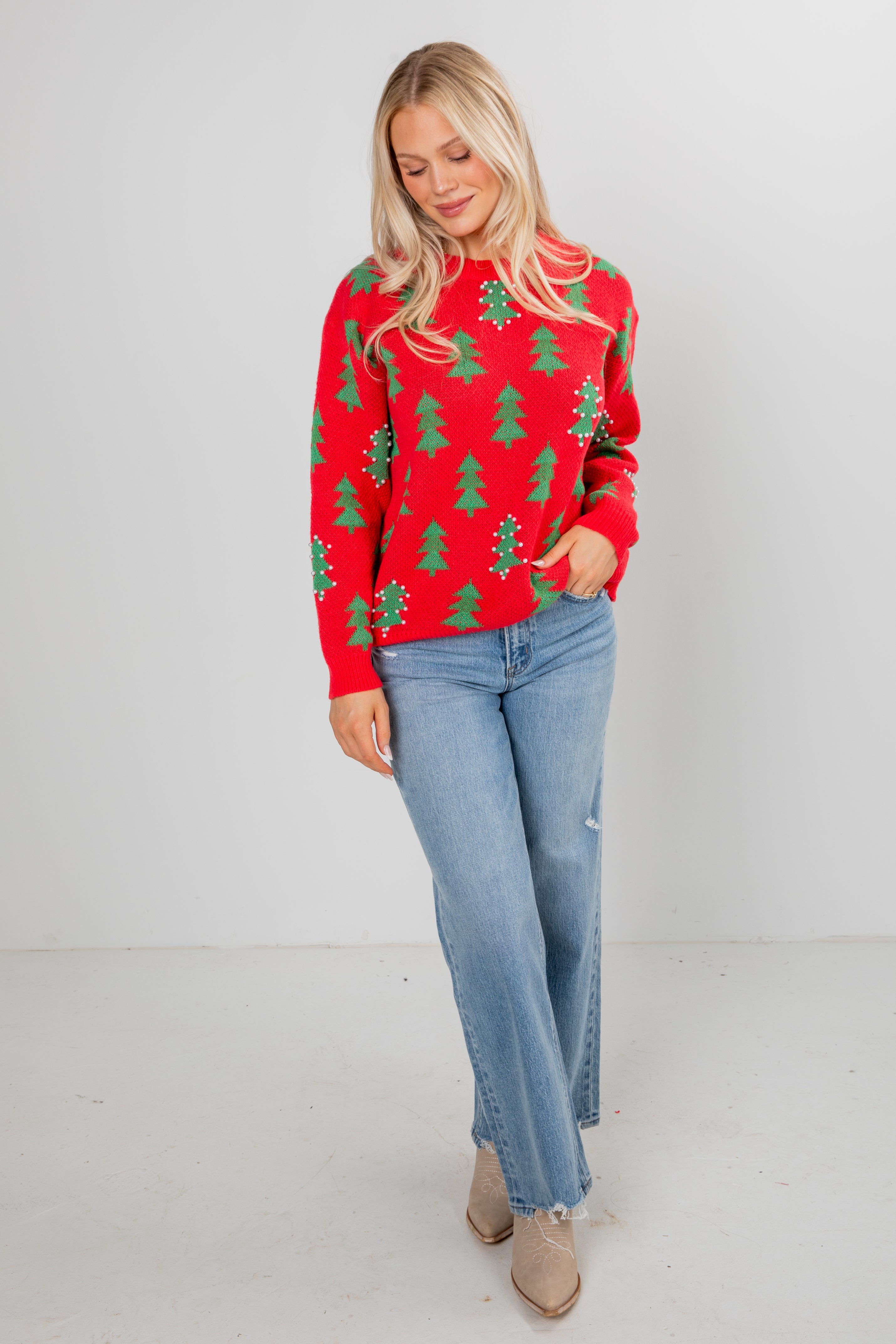 Woman wearing a red sweater with green tree patterns and blue jeans on a white background