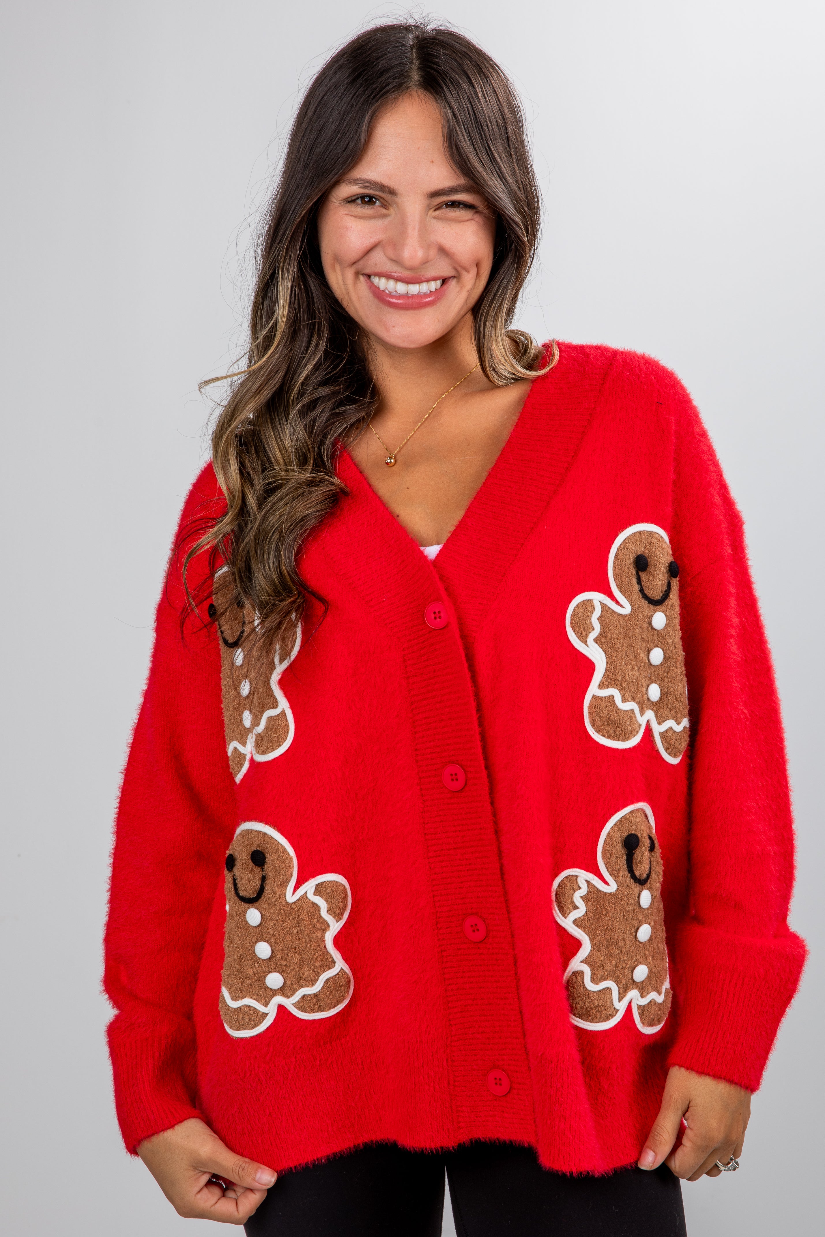 Woman wearing a red cardigan with gingerbread man patterns on a plain background