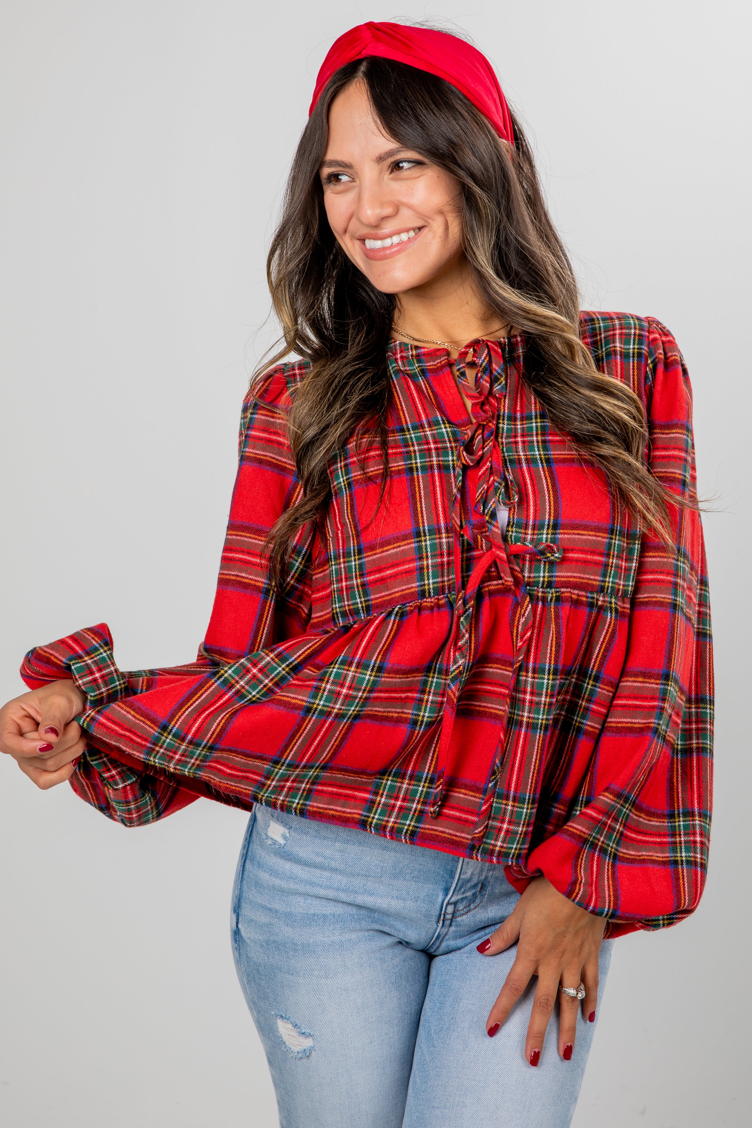 Woman wearing a red plaid blouse and blue jeans against a gray background