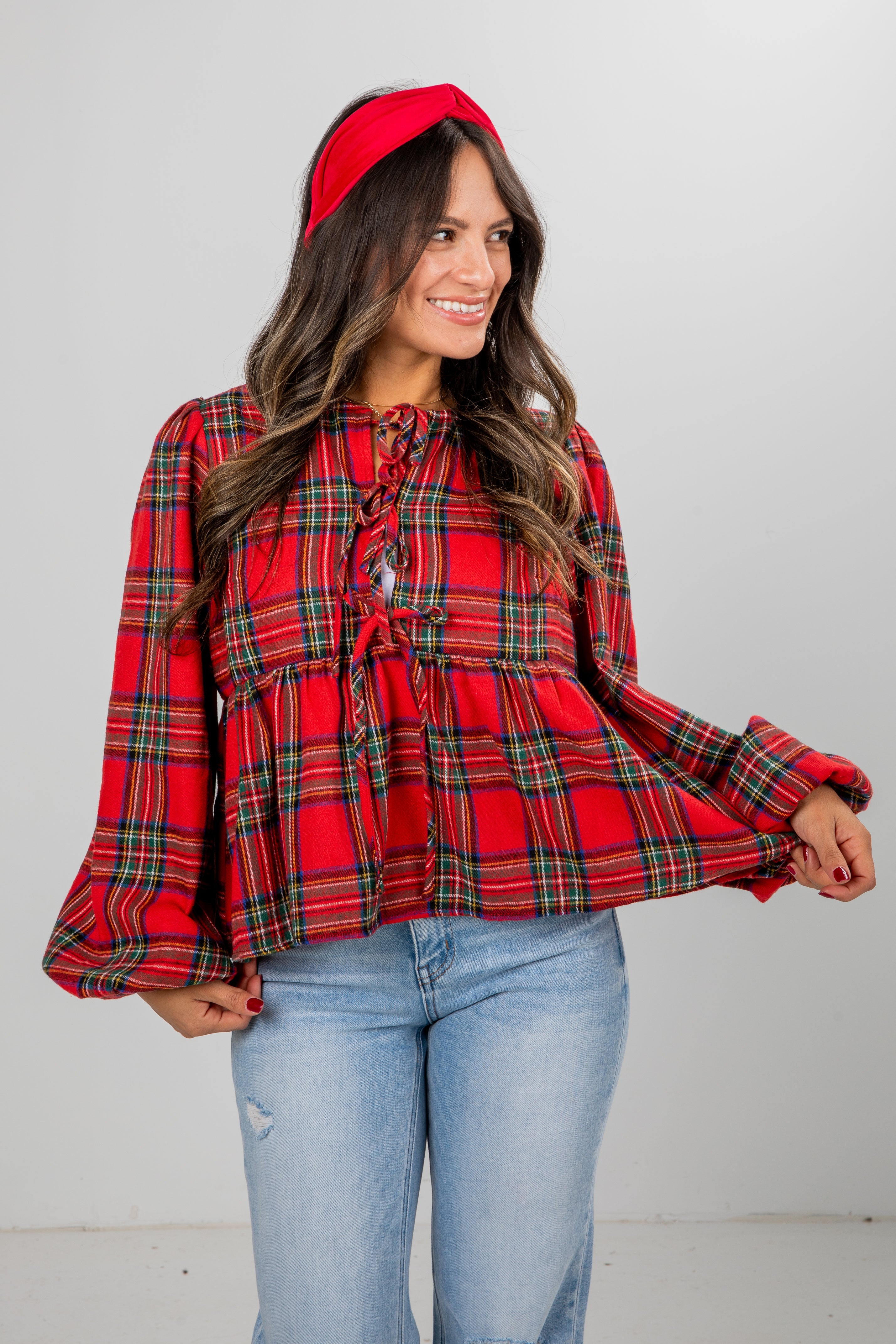 Woman wearing a red plaid blouse and blue jeans against a gray background