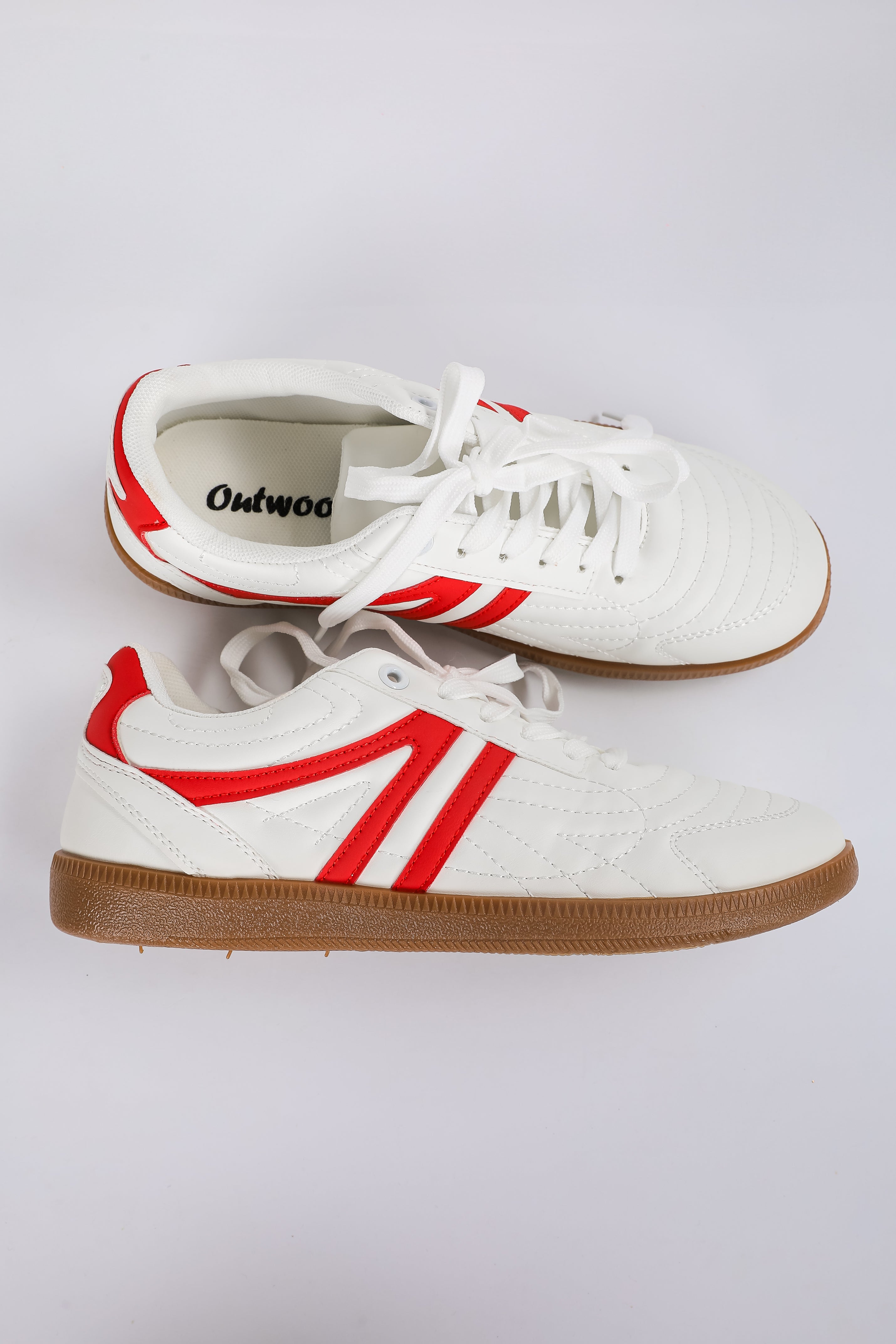 White sneakers with red accents and brown soles on a light gray background