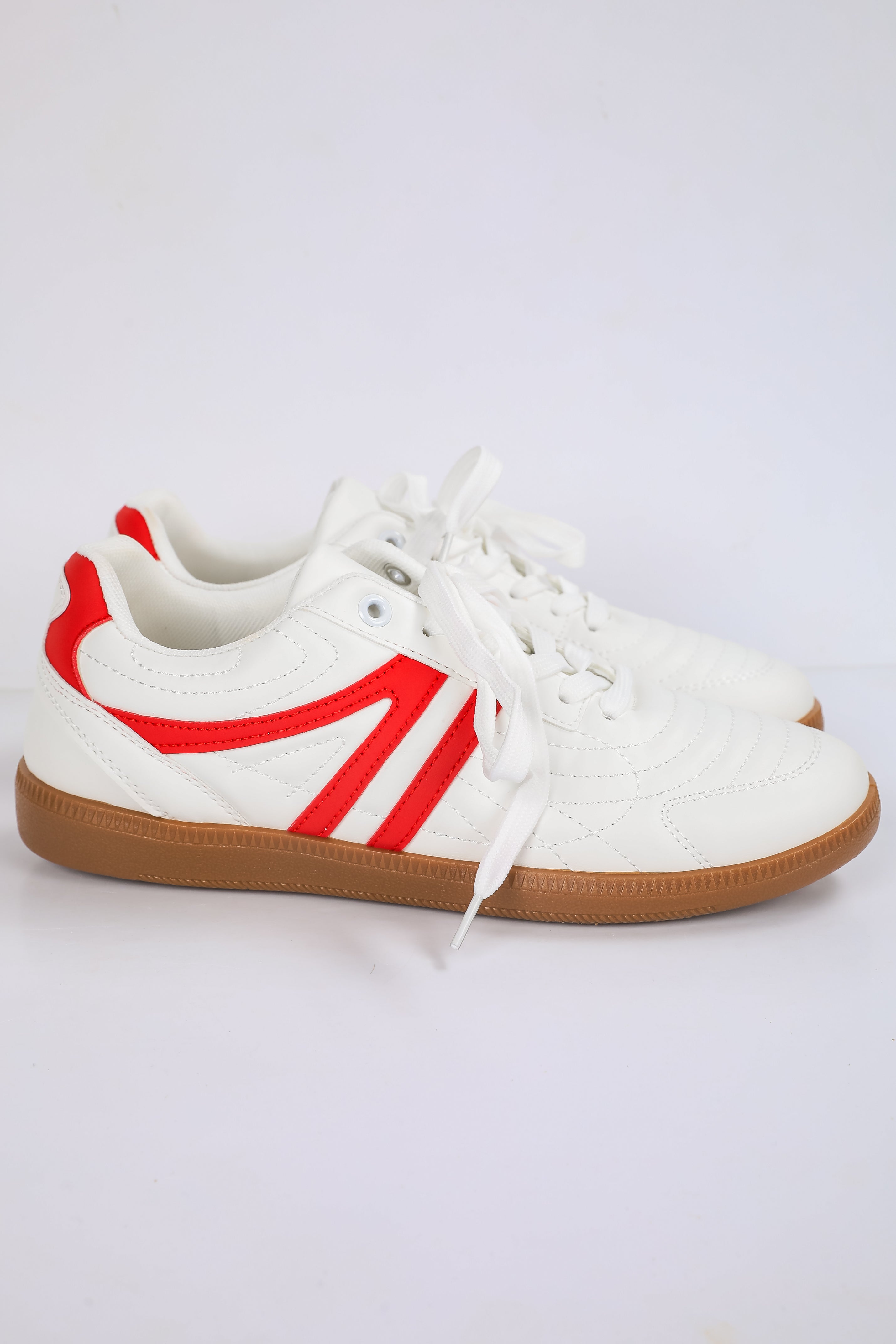 White sneakers with red accents and brown soles on a light gray background