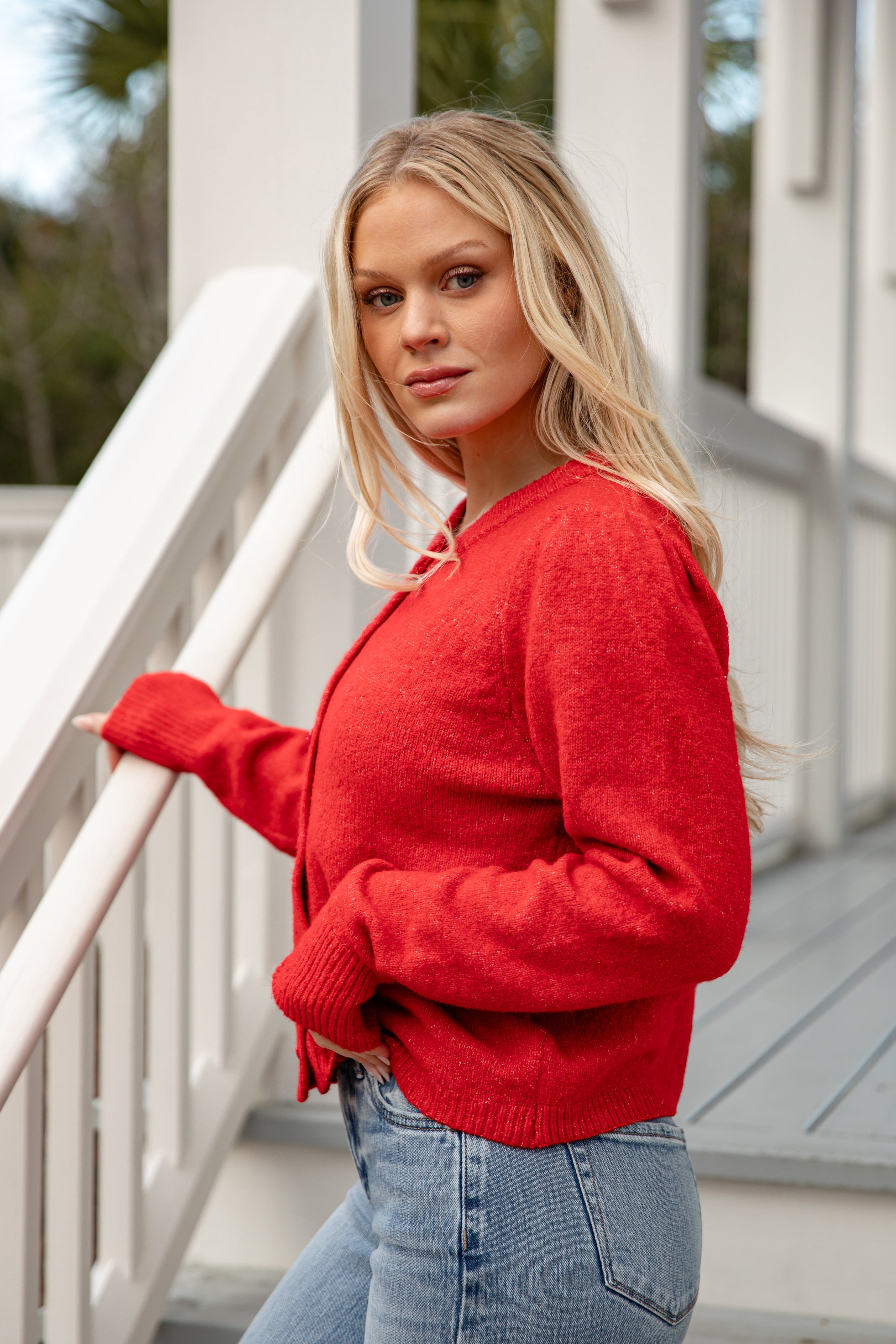 Woman wearing a red sweater and blue jeans standing on a staircase.