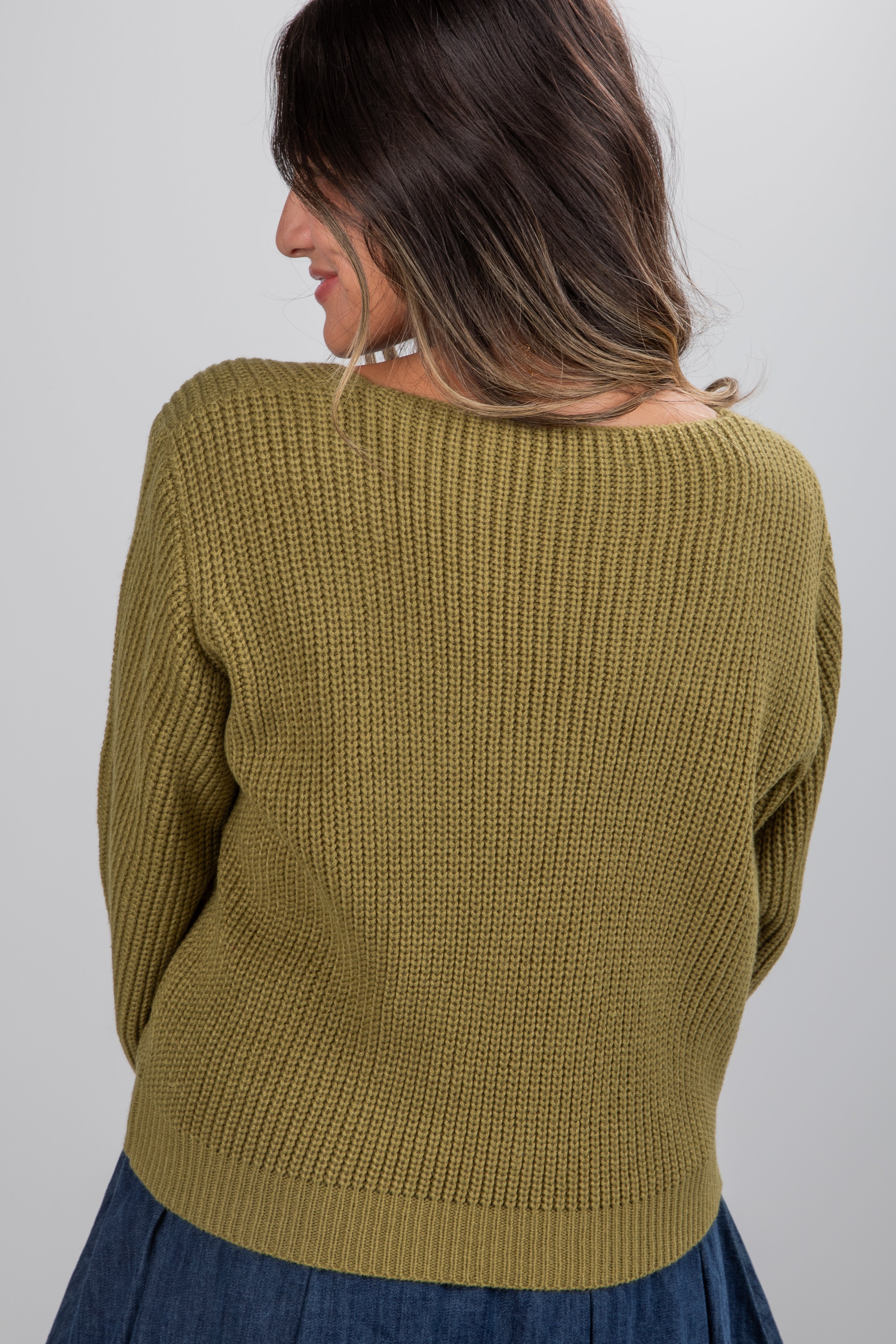 Woman wearing a green knitted sweater against a plain background
