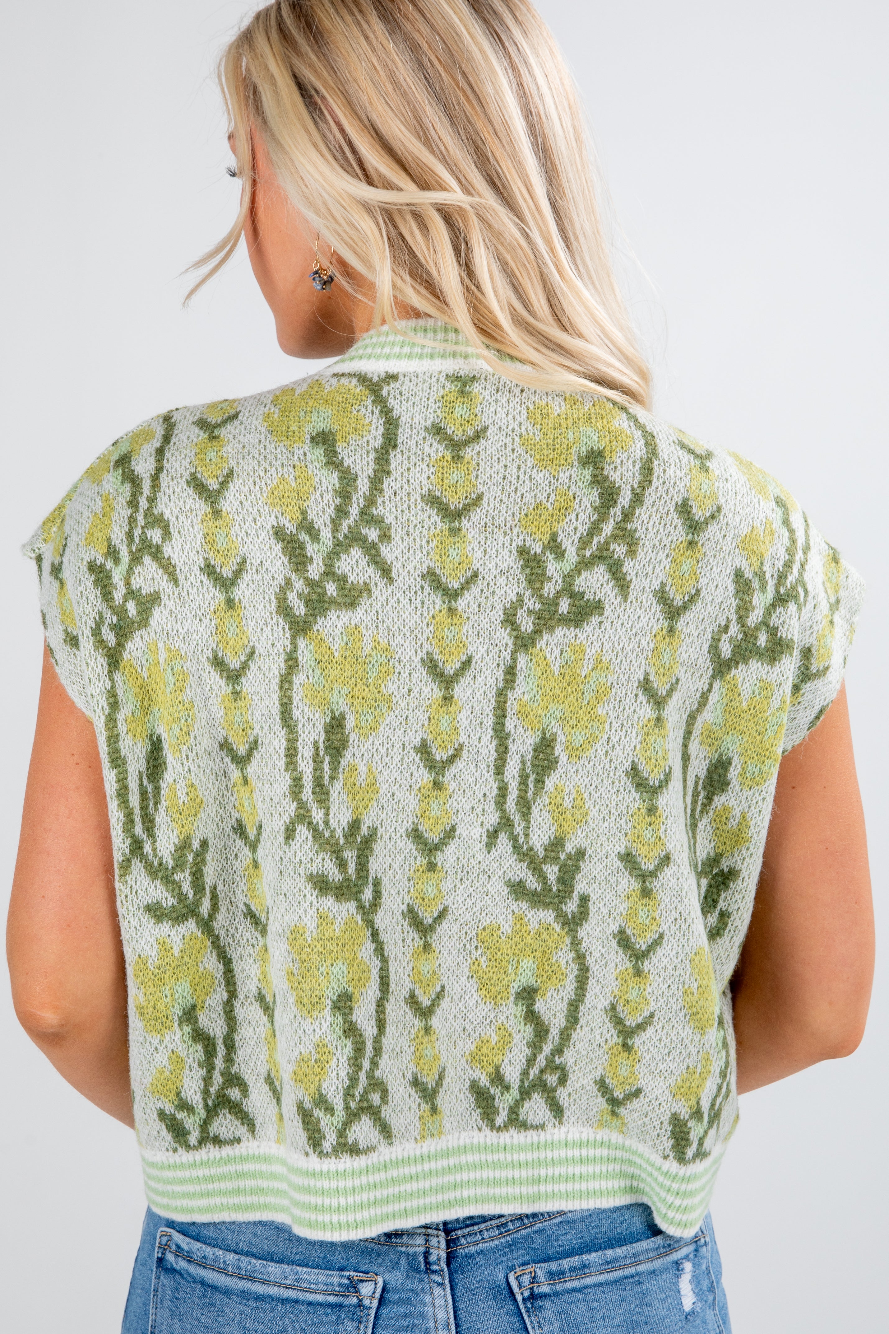 Woman wearing a sleeveless knitted vest with floral pattern on a plain background