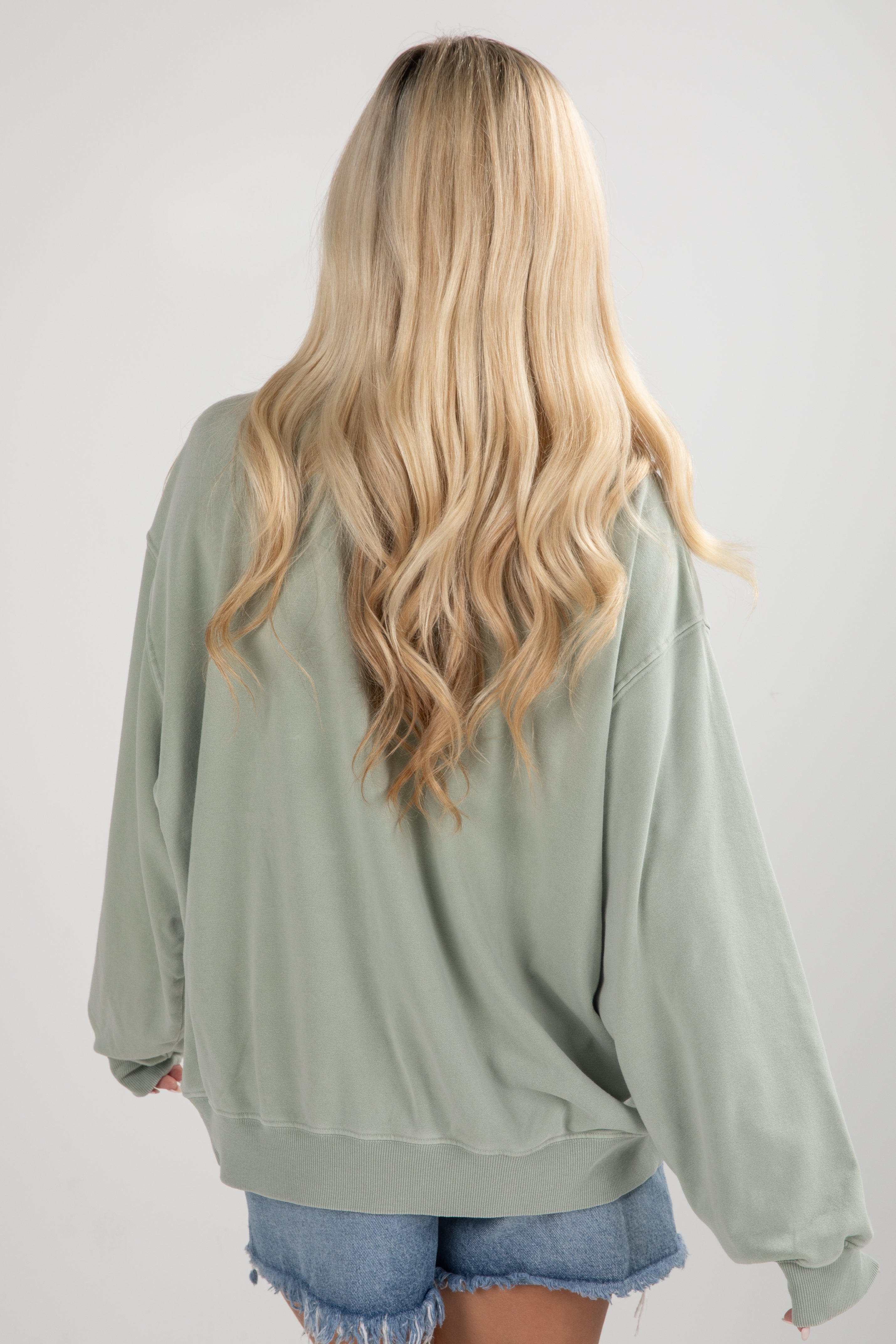 Person wearing a light green oversized sweater with long blonde hair on a white background